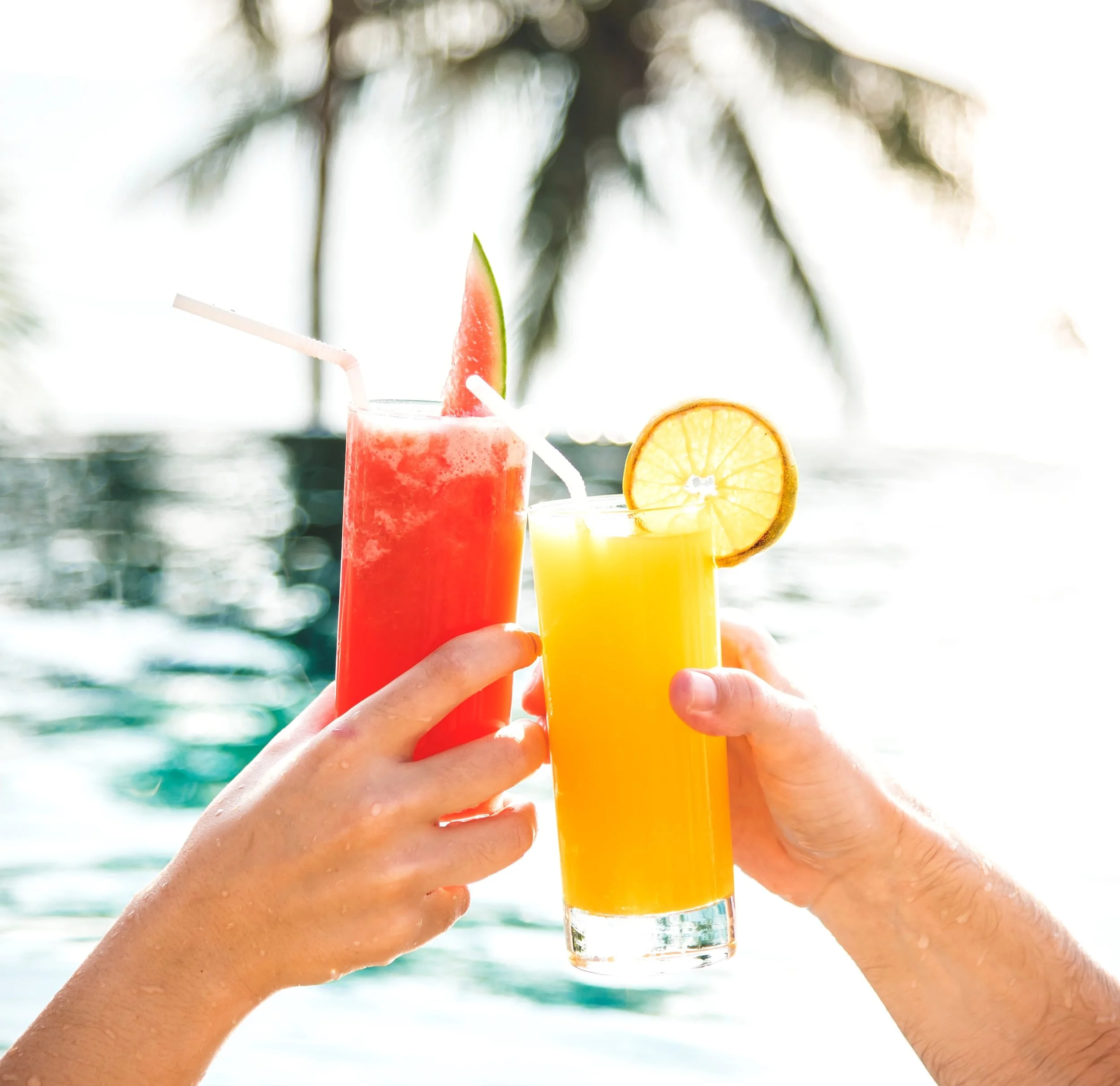 Hands holding glasses full of colorful drinks and clinking them together.