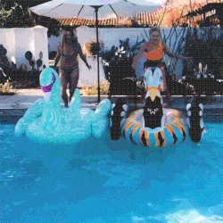 Two women jumping on and surfing pool toys.
