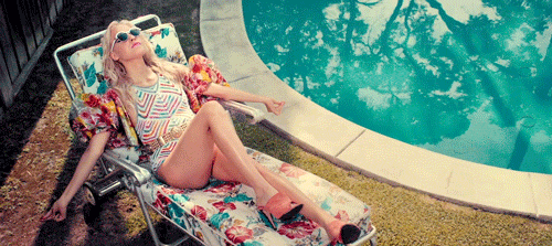 A woman shaking her shoulders on a pool chair next to a pool.