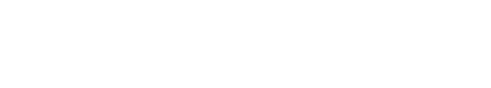 A person sitting at a desk working on a computer with a stack of books and potted plants