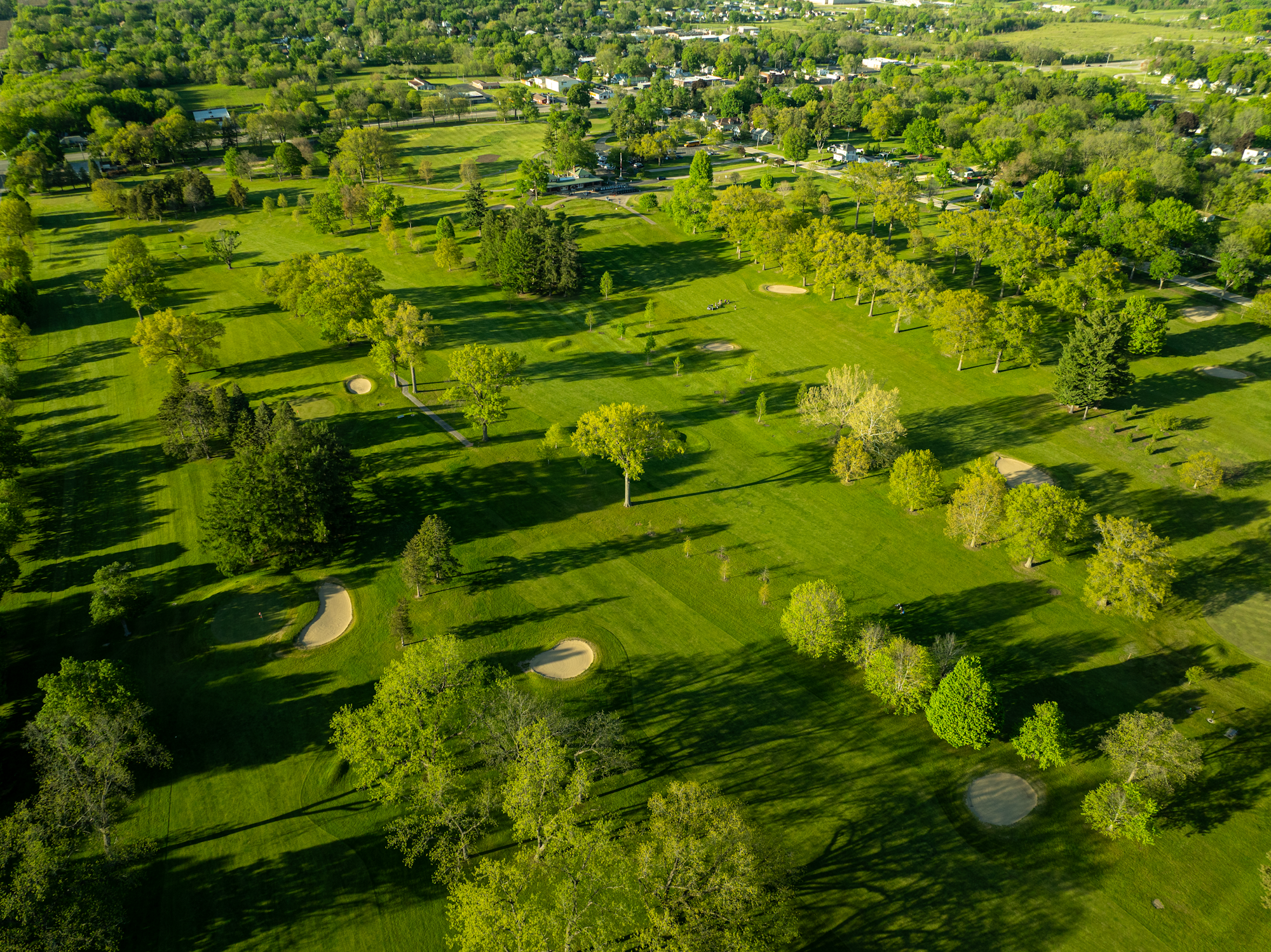 Aerial view of a lush green golf course with trees, sand bunkers, and fairways.