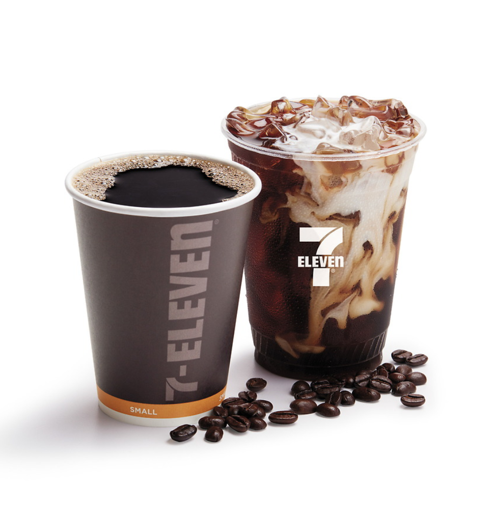A hot black coffee in a gray 7-Eleven cup and an iced coffee with cream and chocolate syrup in a clear 7-Eleven cup with ice cubes, surrounded by coffee beans.