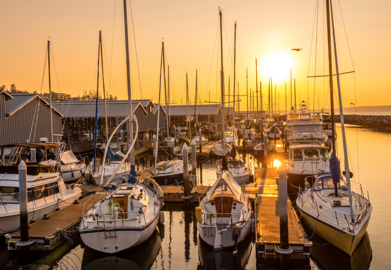 Boats docked at a marina during sunset with orange sky and calm water reflections.