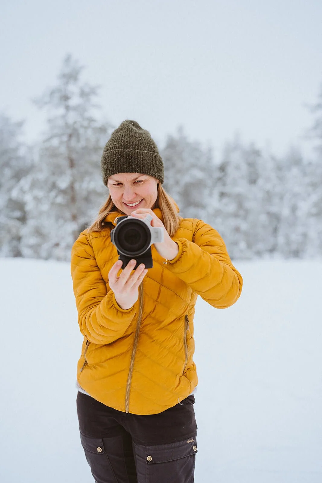 Lapland photographer taking photograph outdoors in a snowy landscape, wearing a yellow jacket and a brown beanie.