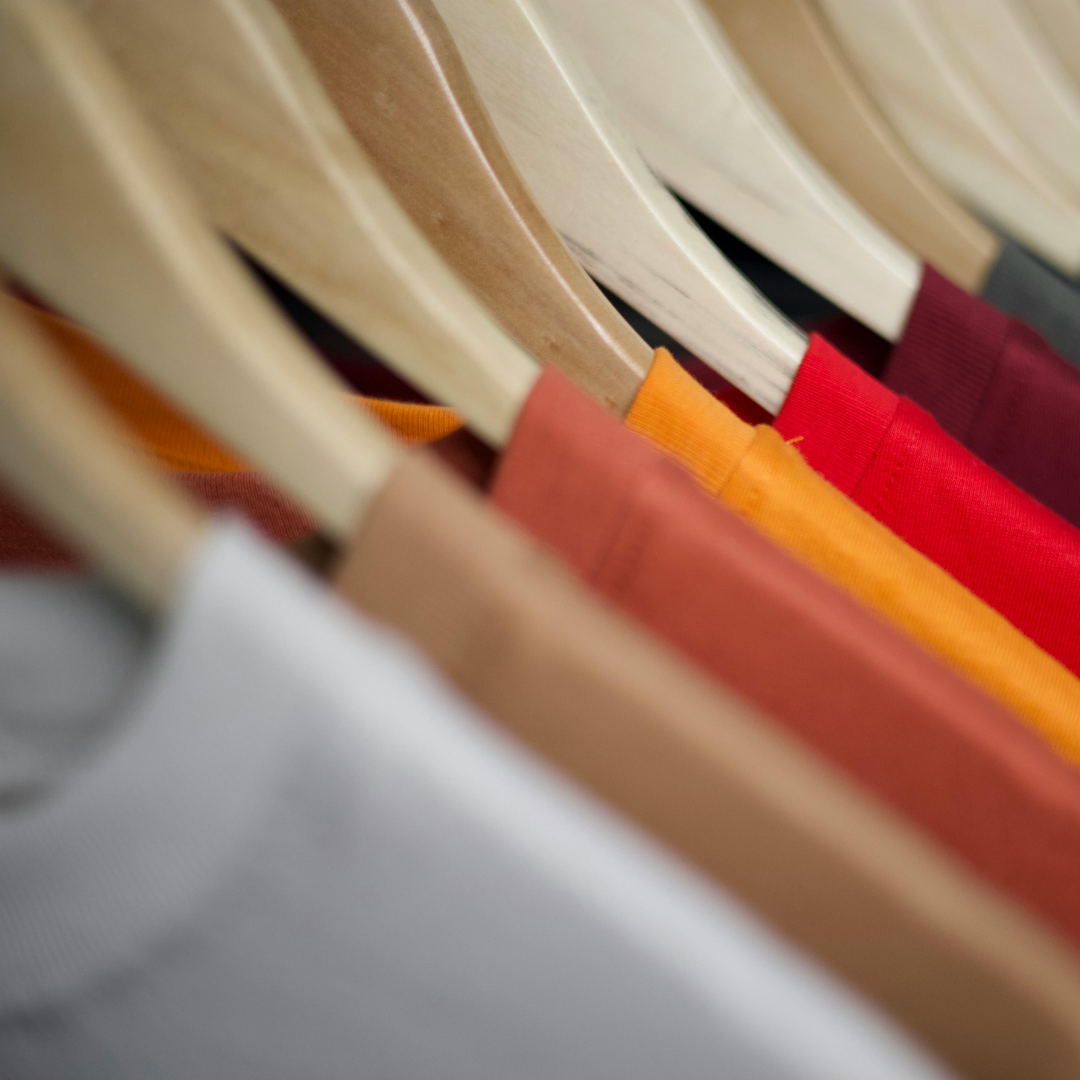 Close-up of hanging clothing on wooden hangers, featuring shirts in various colors including red, orange, maroon, and beige.