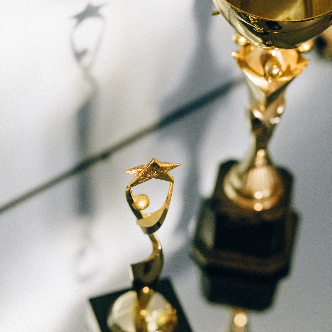 Close-up of two gold trophies with star designs on top, against a blurred background.