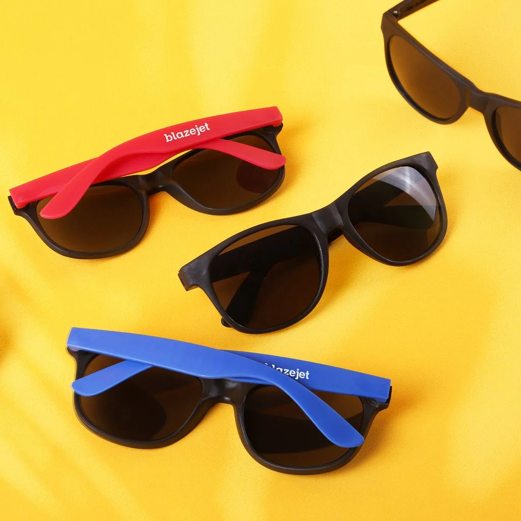 Three pairs of sunglasses with black frames and dark lenses on a yellow background, with one pair featuring a red and blue strap.