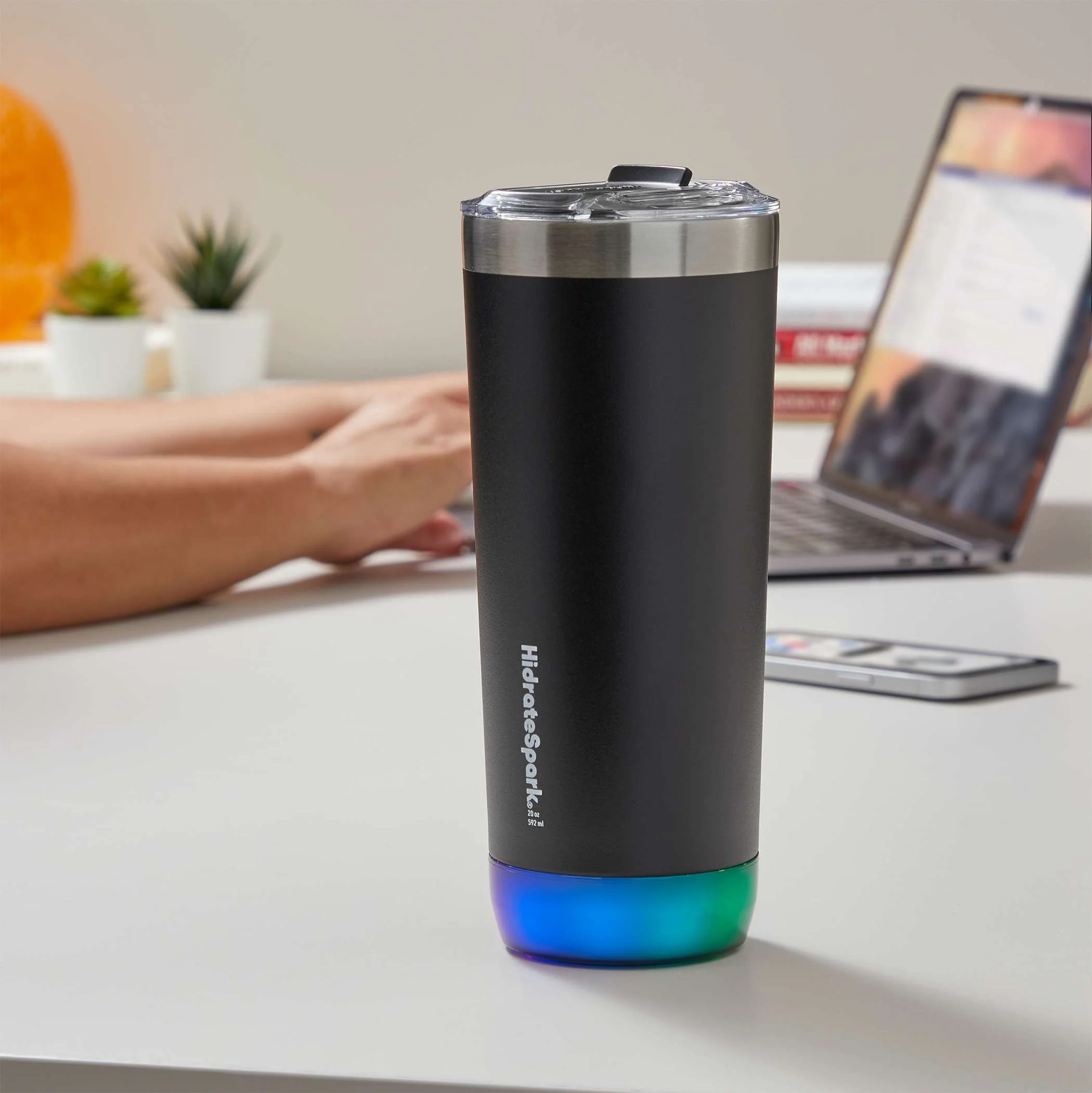 Black insulated tumbler with a colorful glow at the bottom, on a white table in an office setting.