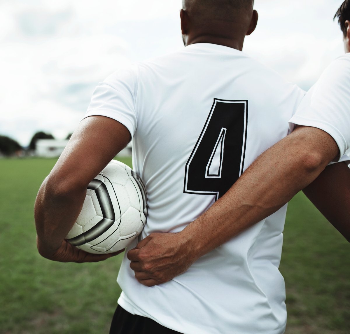 Soccer player wearing a white jersey with the number 4, holding a soccer ball under his arm, on a grassy field.