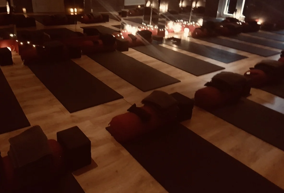 A softly lit, warm room with yoga mats, bolsters and eye pillows laid out