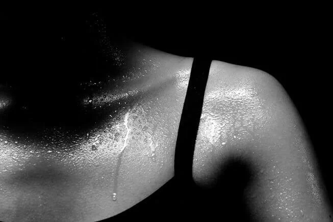 Close-up of a person's shoulder and neck with water droplets on their skin, wearing a strap  Absolute Yoga Crosby.