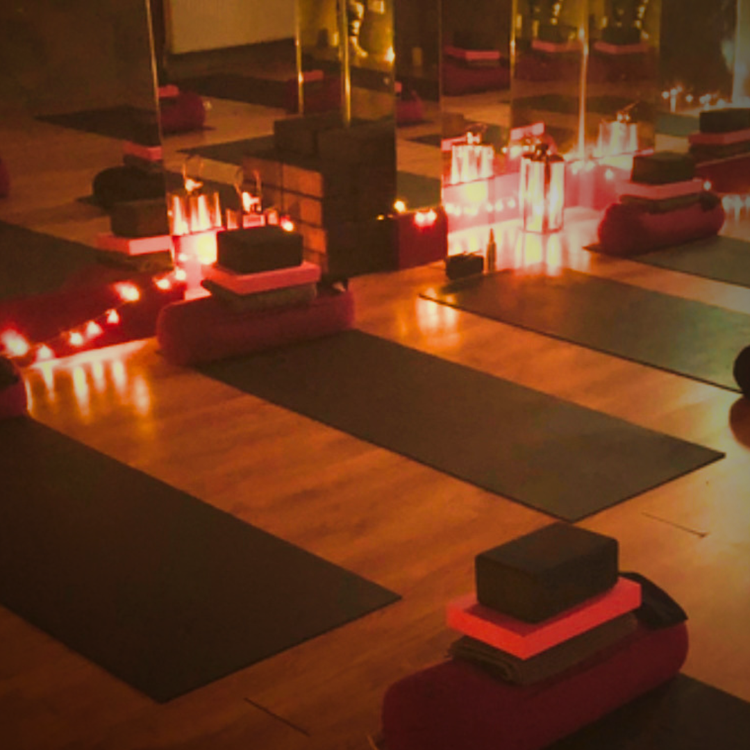 A softly lit, warm room with yoga mats, bolsters and eye pillows laid out