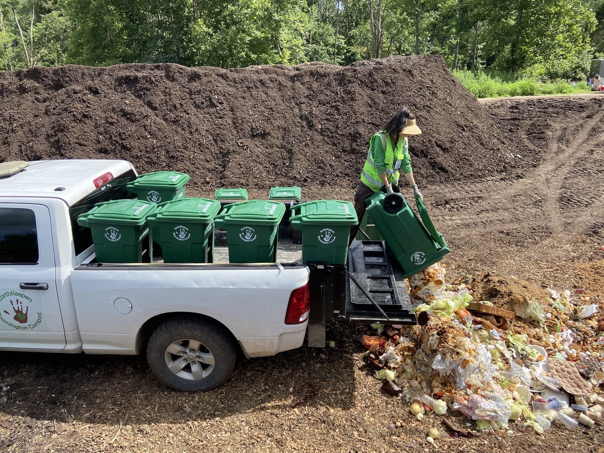 EarthKeepers Staff emptying a compost bin on a large pile of compost at their facility