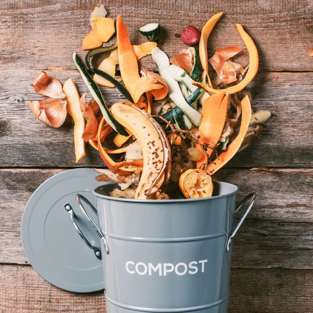 Kitchen compost bin laying on its side on a rustic wooden table with produce scraps
