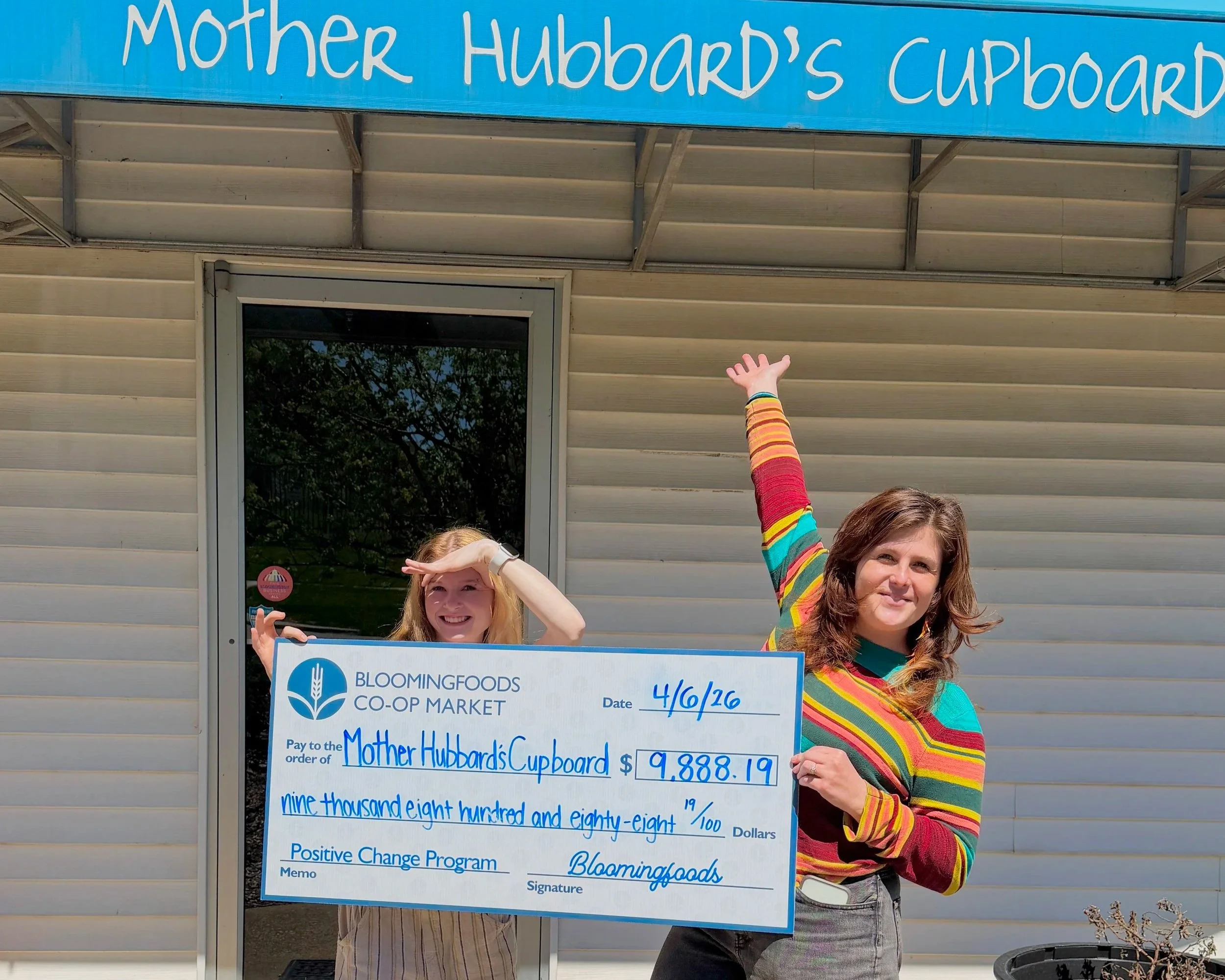 Mother Hubbard's Cupboard staff standing in from on their building, holding the big check for the funds raised for them through our 2026 Positive Change program