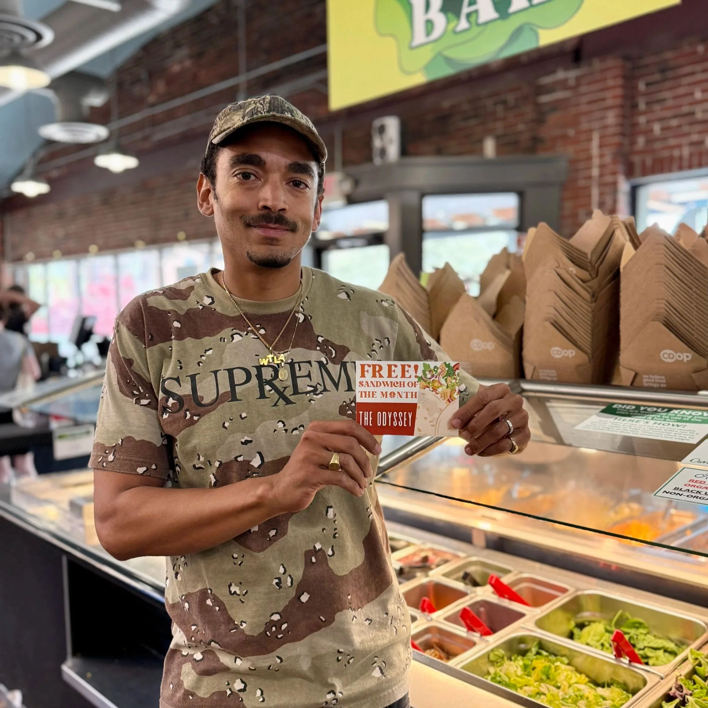 Tyler sanding next to our Near West Store's salad bar holding a Free Sandwich of the Month Card
