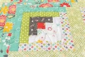 A Log Cabin Quilt scare with various fabrics and a red square in the middle