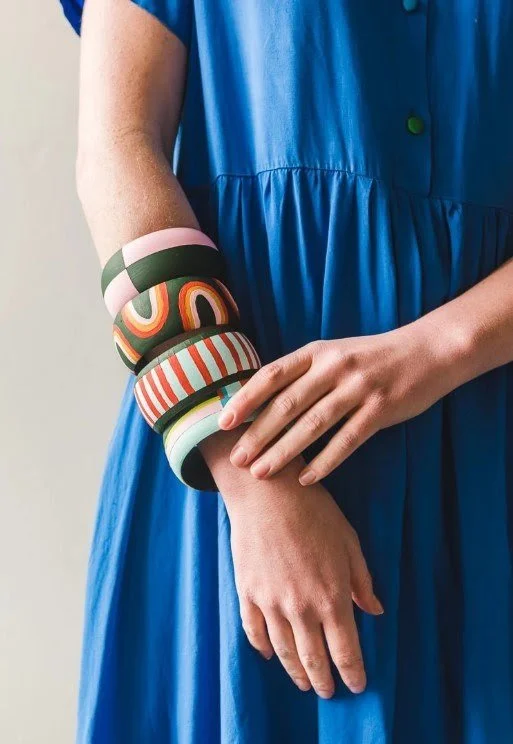 A thin white woman in a blue dress wears four colorful wooden bangles on her wrist