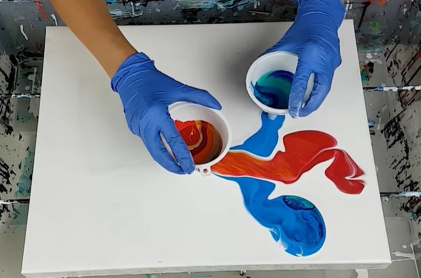 A white woman wearing blue gloves moves red and white paint across a white background
