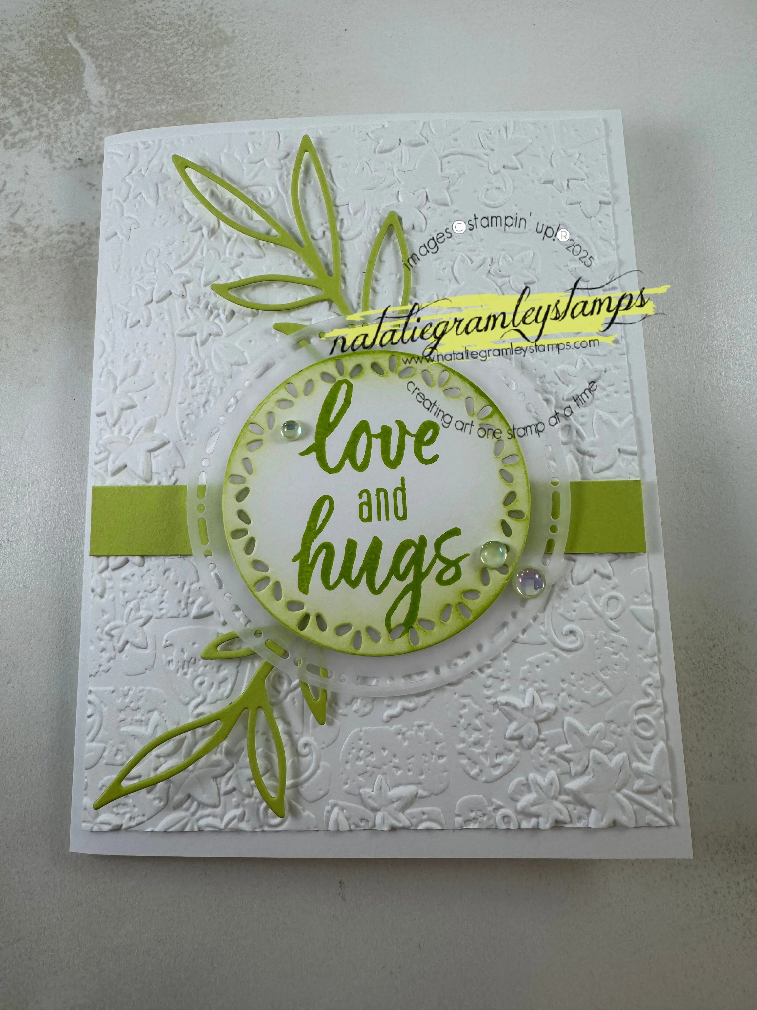A greeting card with chartruese accents and words in a circle in the middle that says Love and Hugs