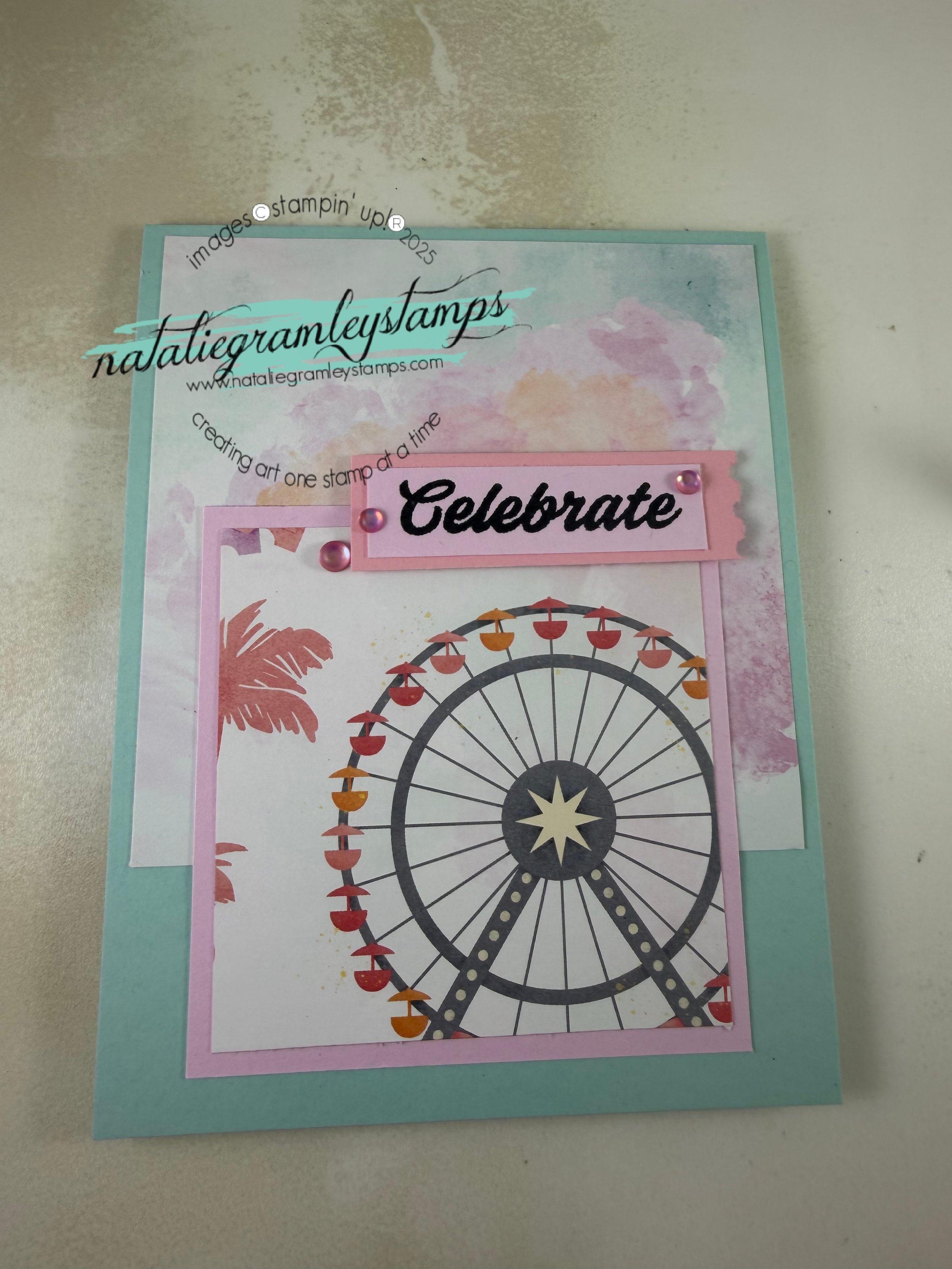 A greeting card in light blues and pinks with a ferris wheel on it. The card says Celebrate!