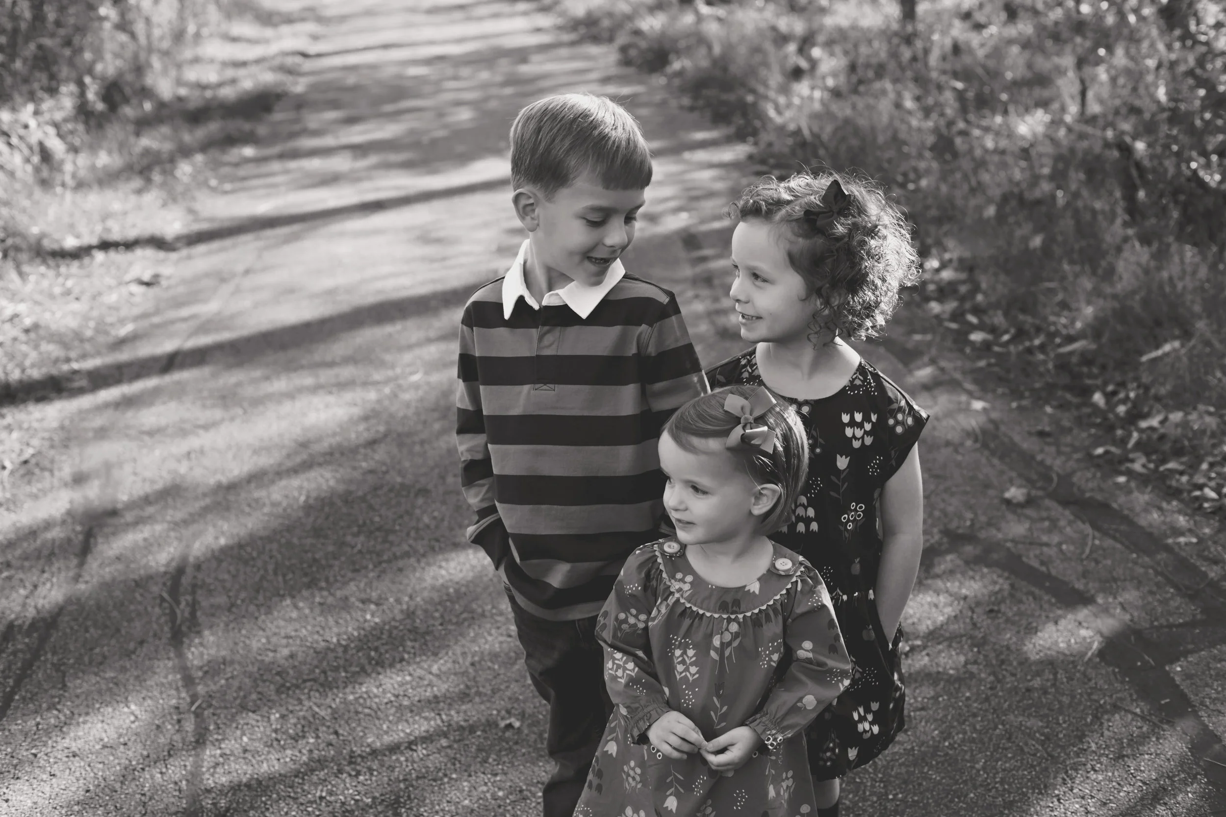 black and white of three siblings talking on a path in the park
