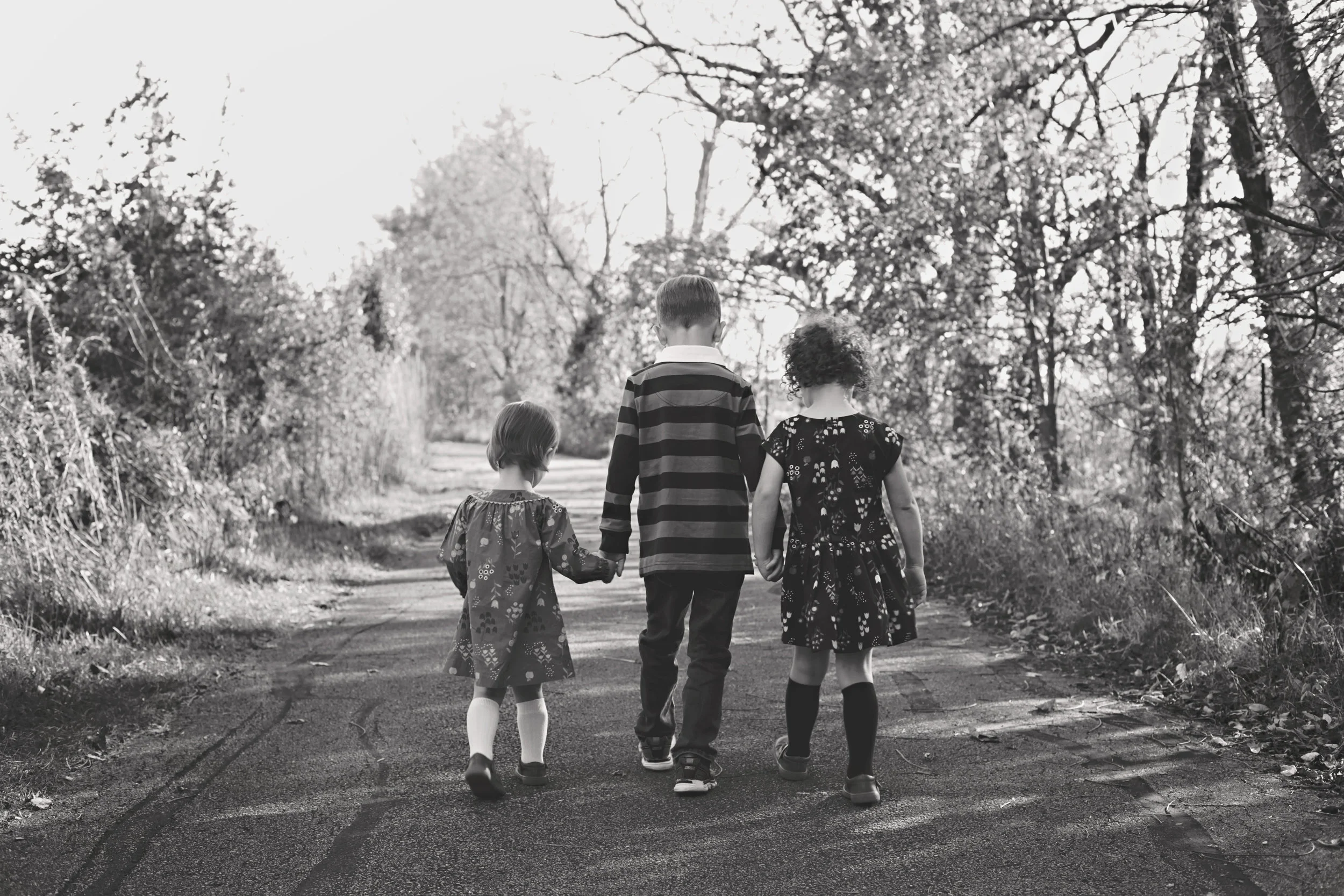 black and white of siblings walking, talking and holding hands in the park