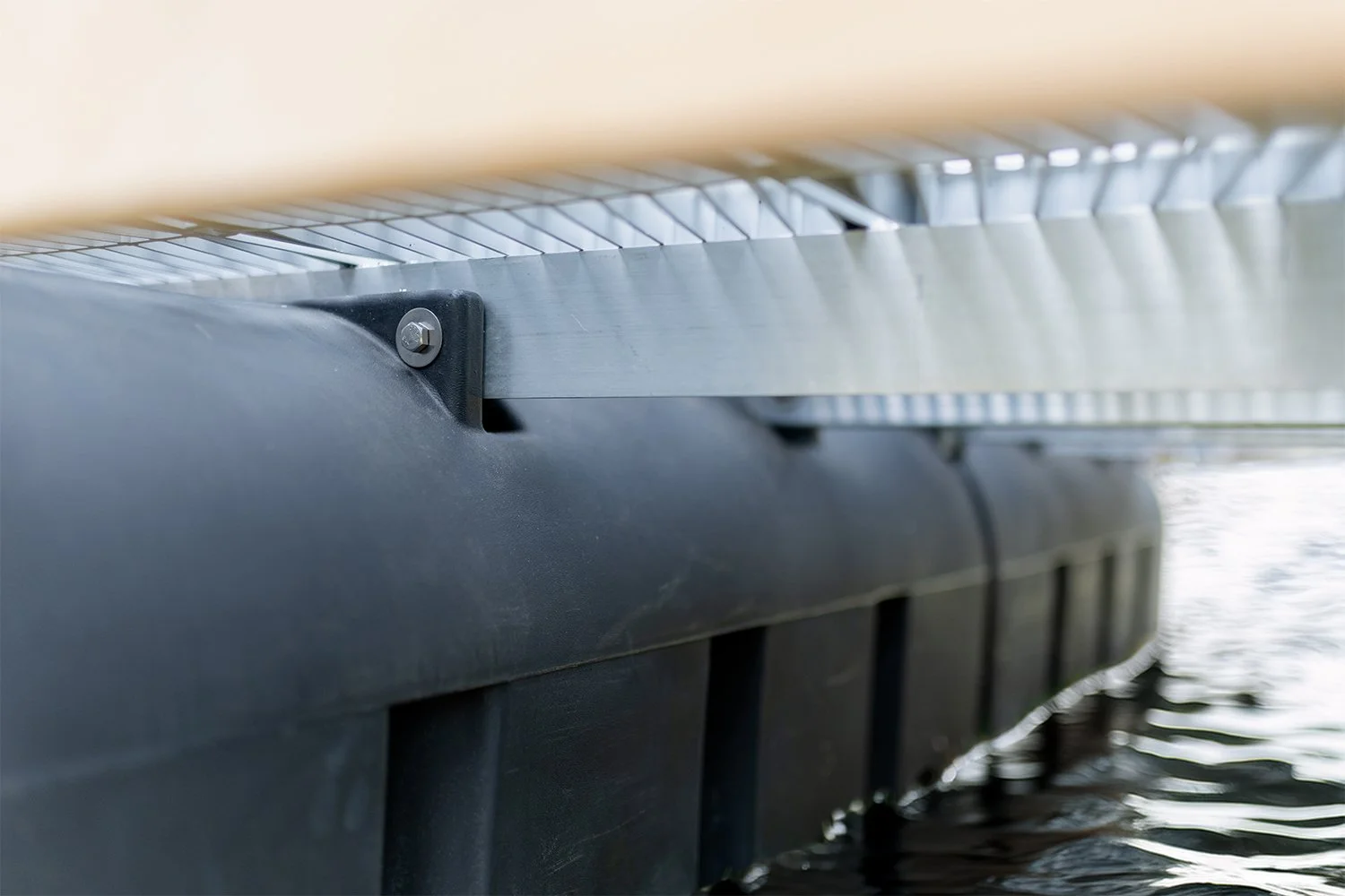 Close-up of the underside of a dock structure using Sturdy Set flotation modules and aluminum joists, floating on water, with water ripples visible at the bottom of the image.