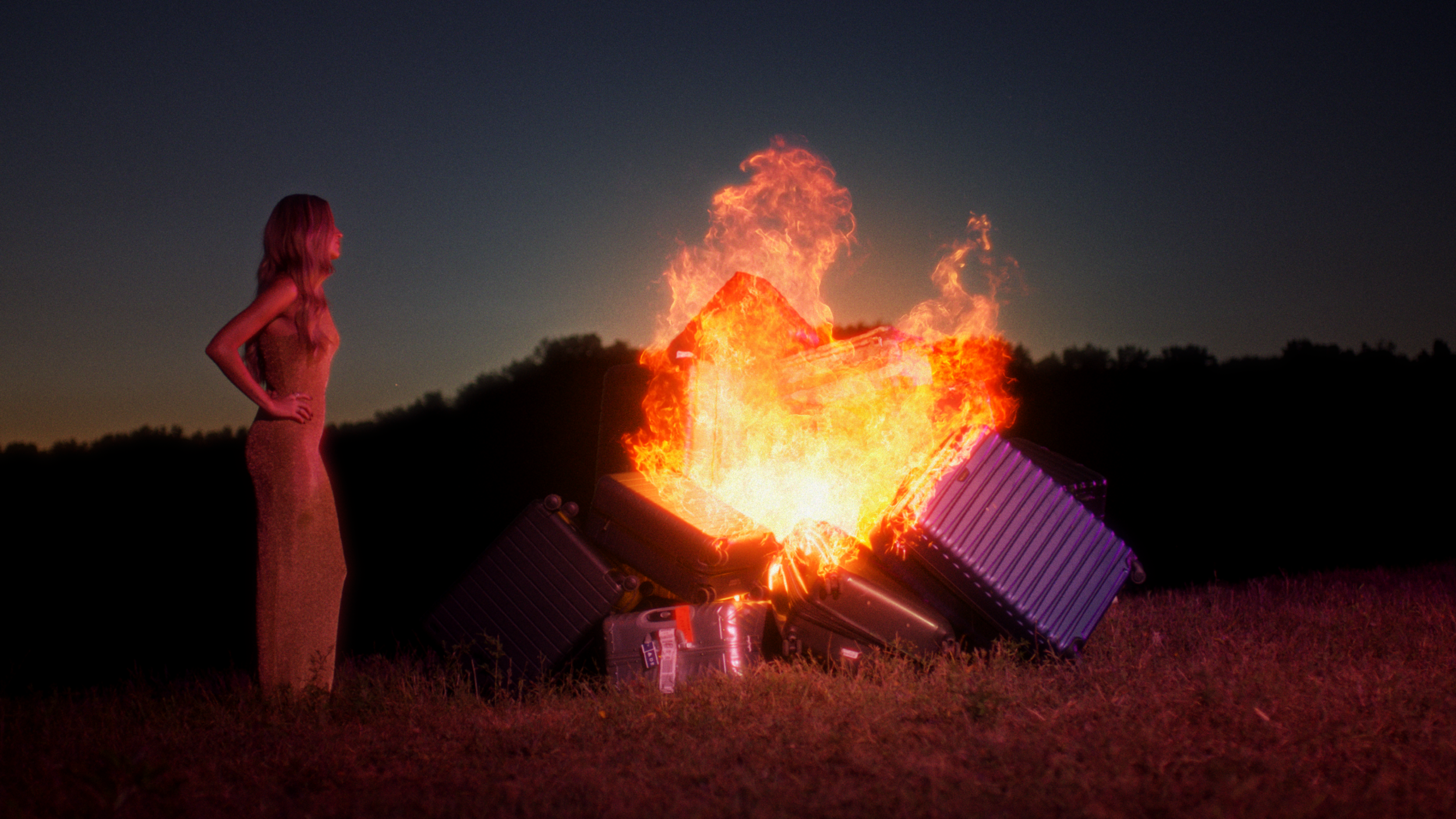 Kelsea Ballerini standing in front of pile of burning suitcase and baggages for her luxury candle campaign