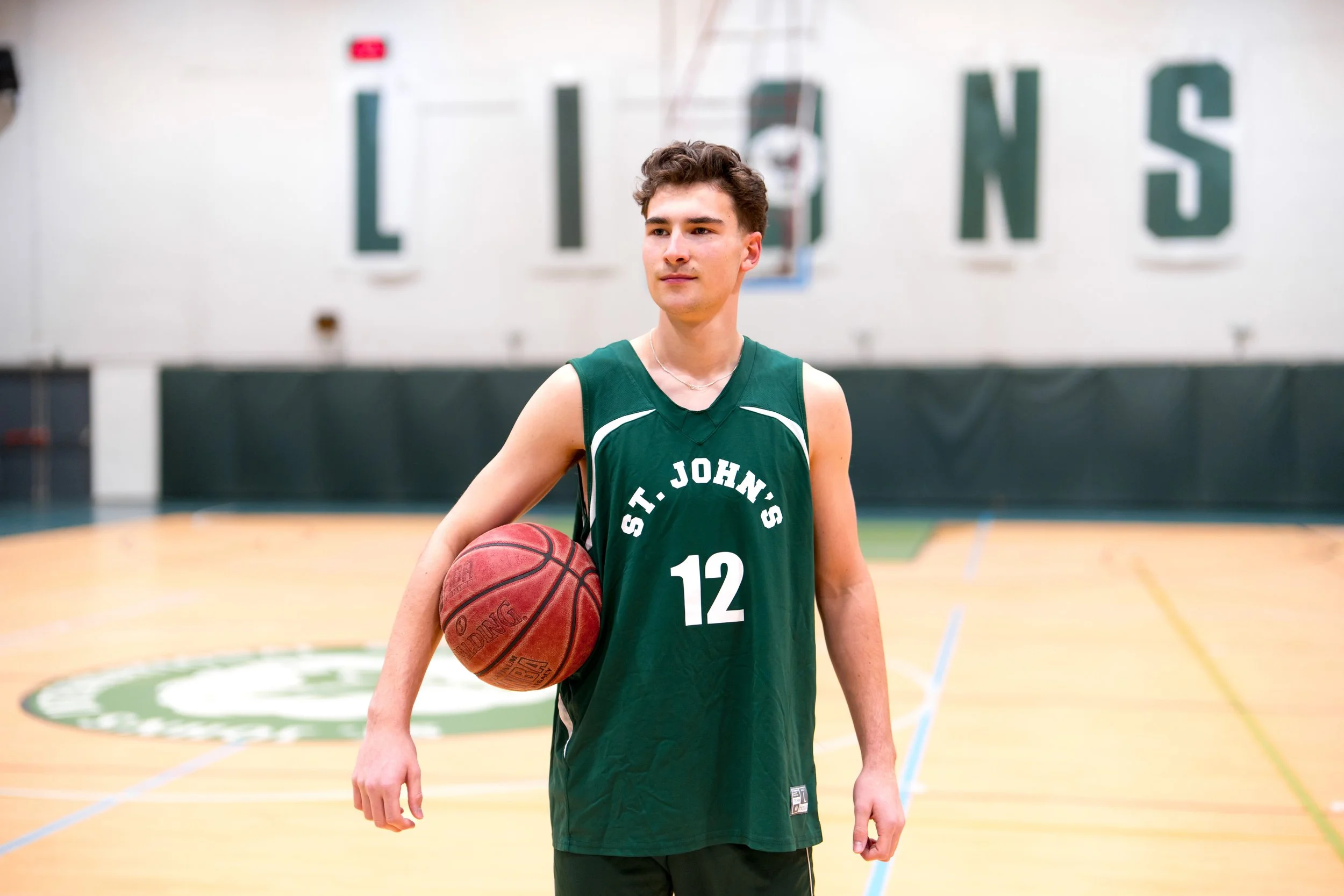 Jeune joueur de basketball portant un maillot vert avec le numéro 12, tenant un ballon de basketball dans un gymnase.