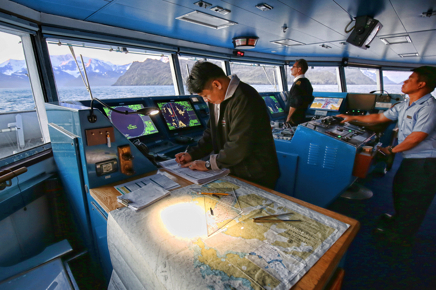From left to right: John, the 2nd officer is making a notion in the ship’s logbook, Captain Eric Saint Plancat has the conn, and Lawrence, the seaman, has the helm.