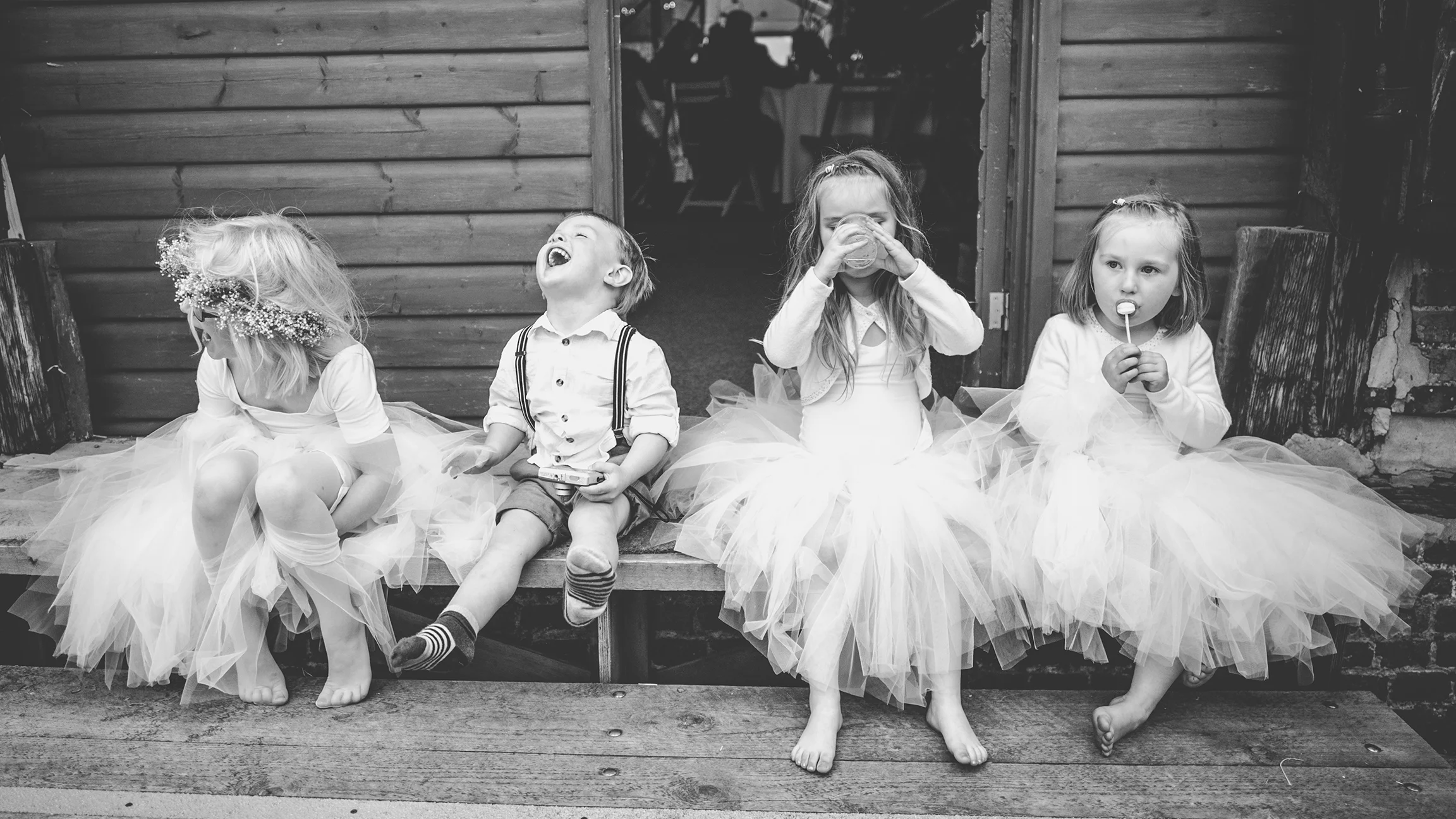 Three flower girls and a page boy sitting on a step, unaware of camera as they laugh eat and drink. Yorkshire wedding photographer.