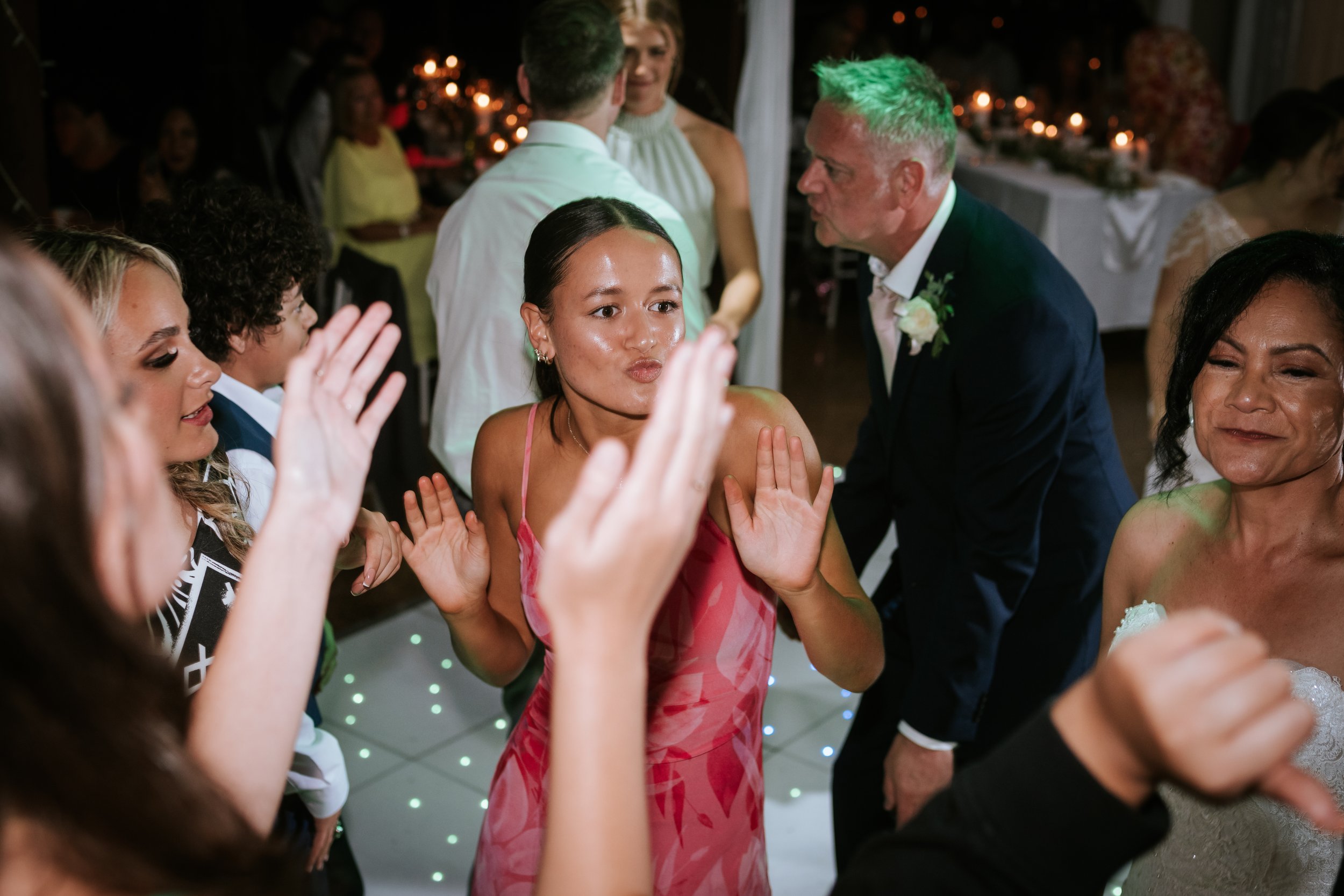 People dancing and celebrating at a wedding reception with warm lighting and floral decor.
