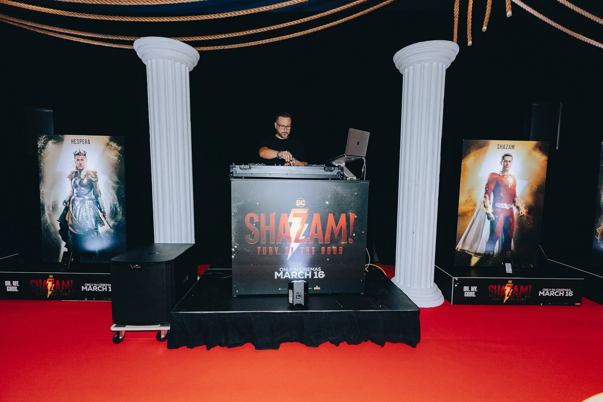 A Beatworks event DJ, DJing at a promotional event for the movie 'Shazam! Fury of the Gods,' with posters of the movie on either side of him.