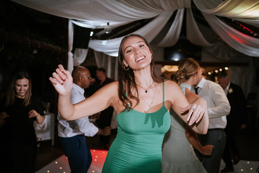 A woman in a green dress smiling and dancing at a party with other guests in the background.