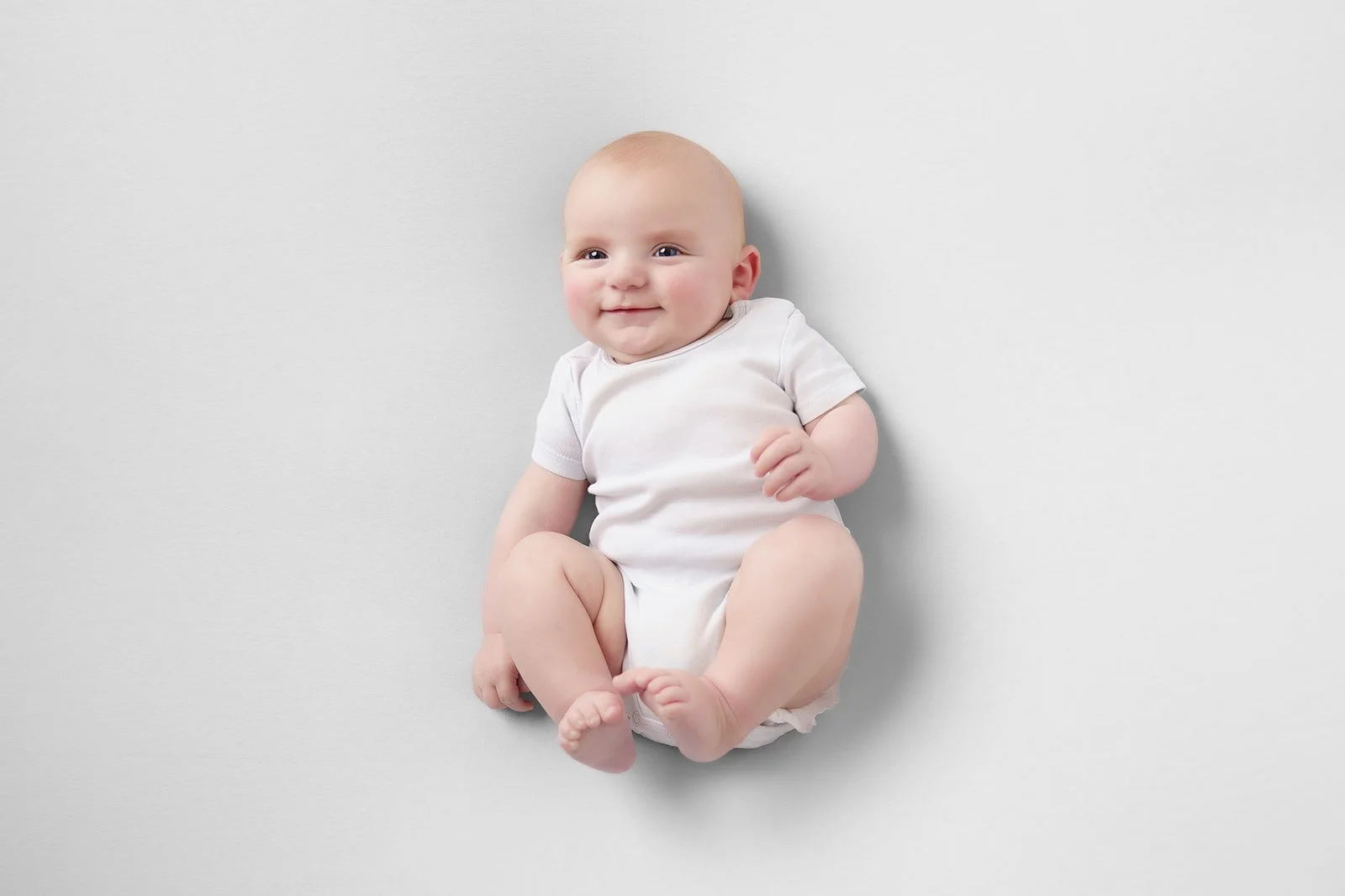 Baby met beentjes in de lucht, tegen een witte achtergrond
