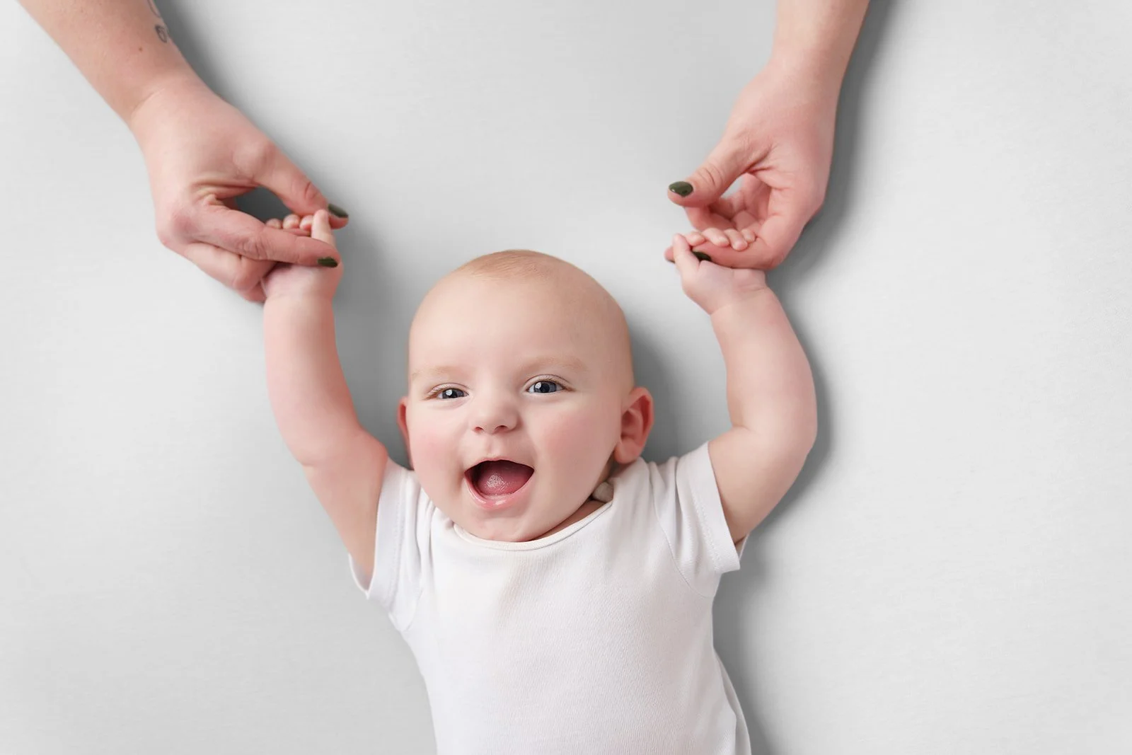 Mama heeft handen vast van baby, die lacht tegen een witte achtergrond
