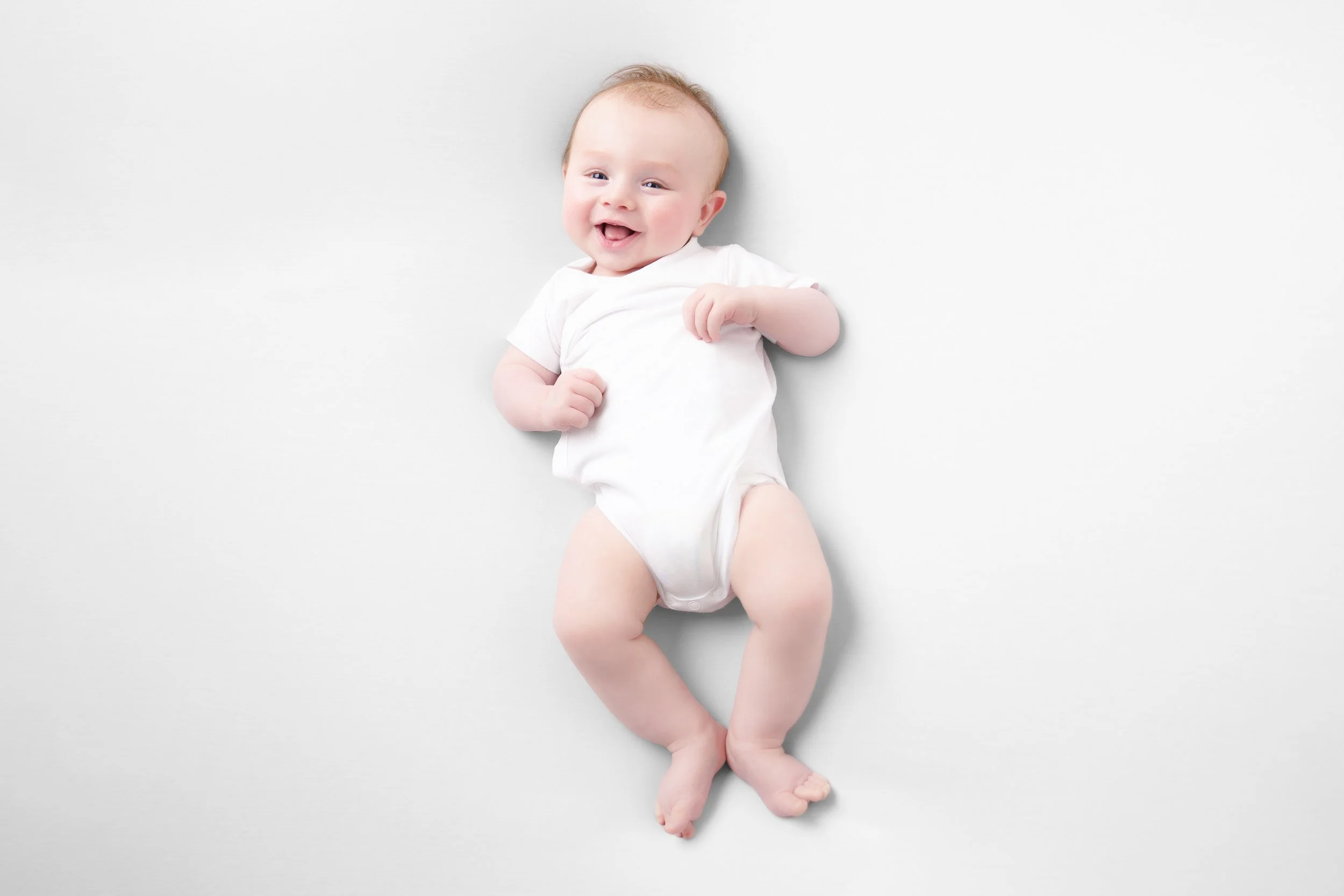 baby in witte romper op zijn rug op een witte achtergrond