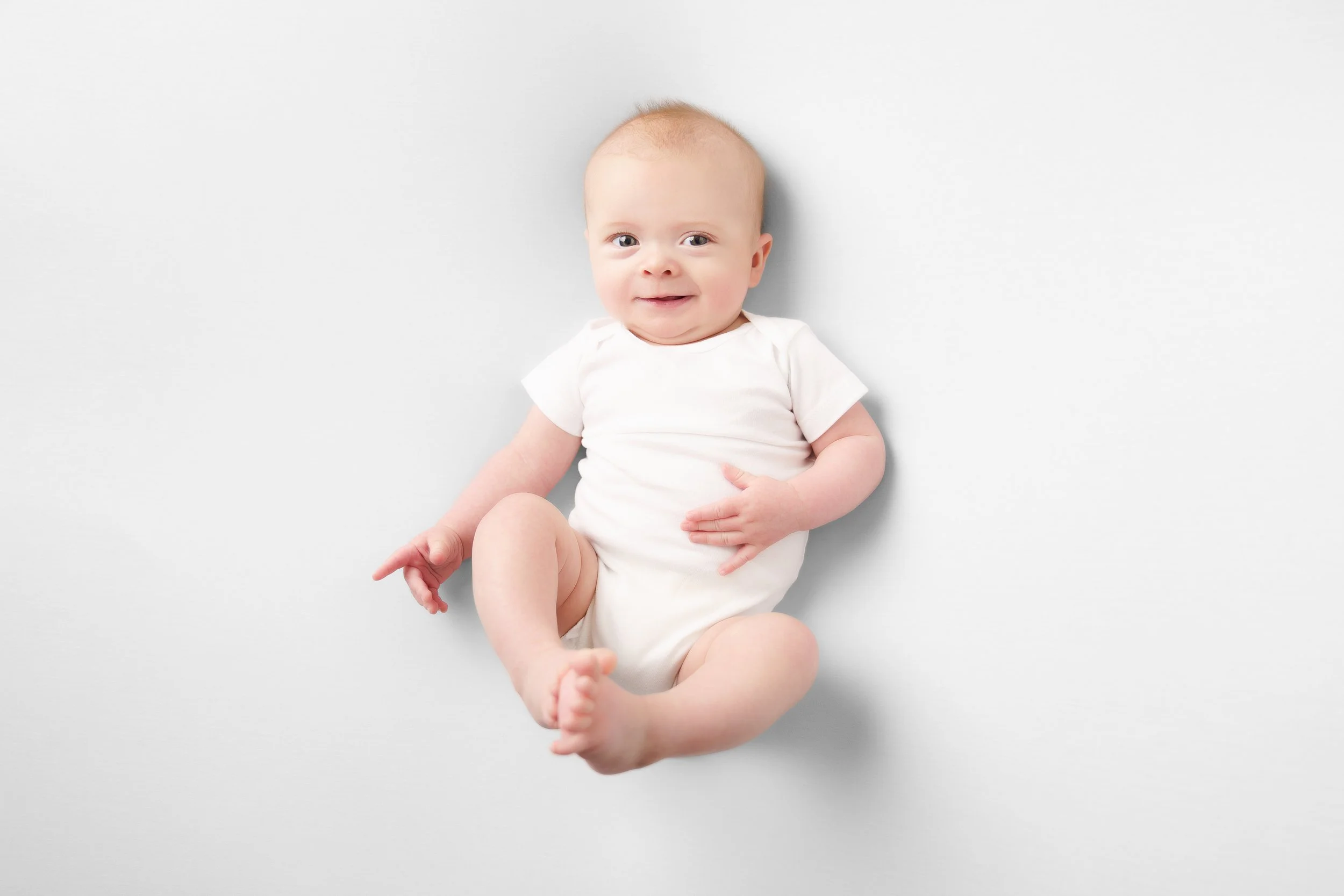 baby in witte romper op zijn rug op een witte achtergrond