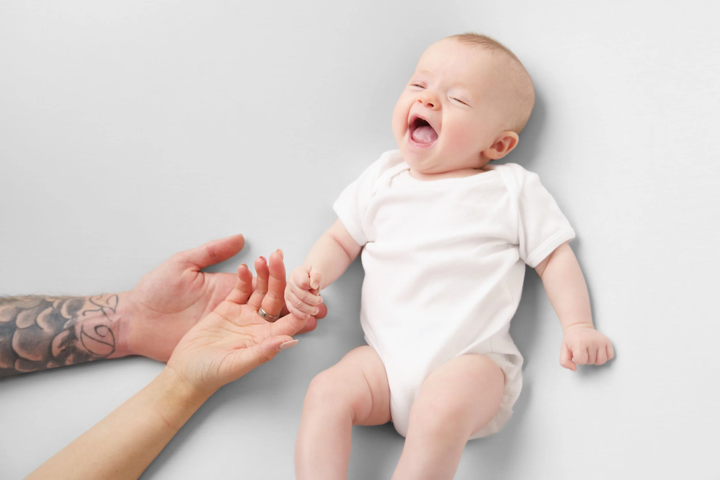 Baby heeft handen van ouders vast en lacht tegen een witte achtergrond