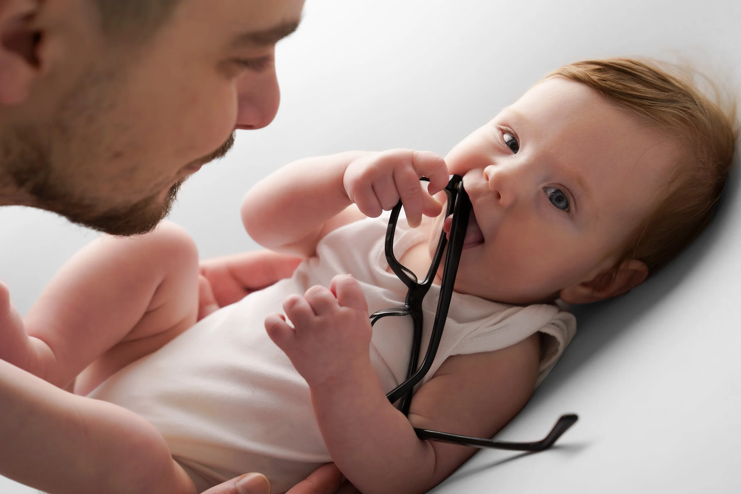 Een baby speelt met papa’s bril, een intiem moment vol nieuwsgierigheid.