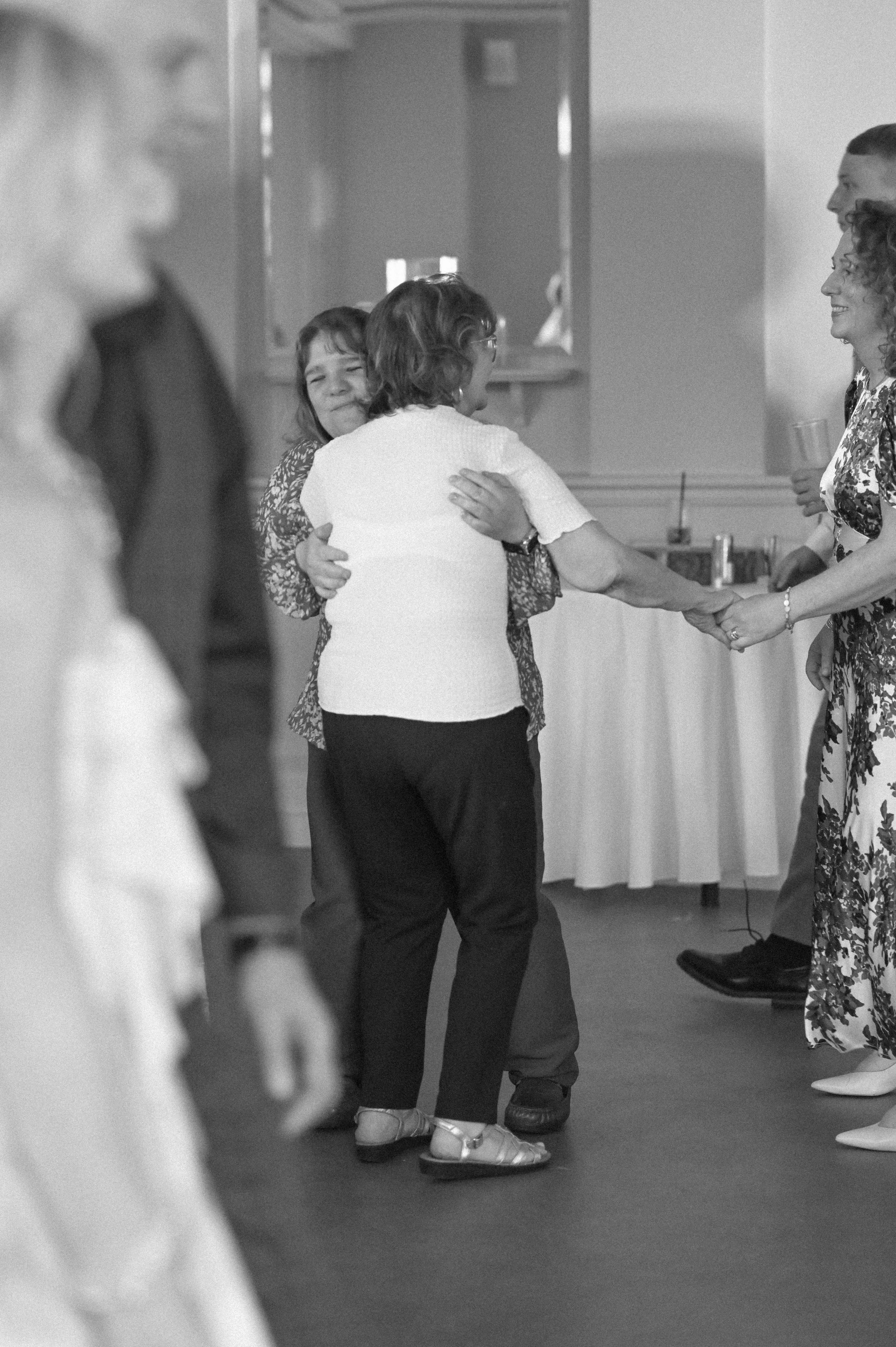 A black and white photograph at The Orangery of wedding guests, white men and women, embracing as they dance.