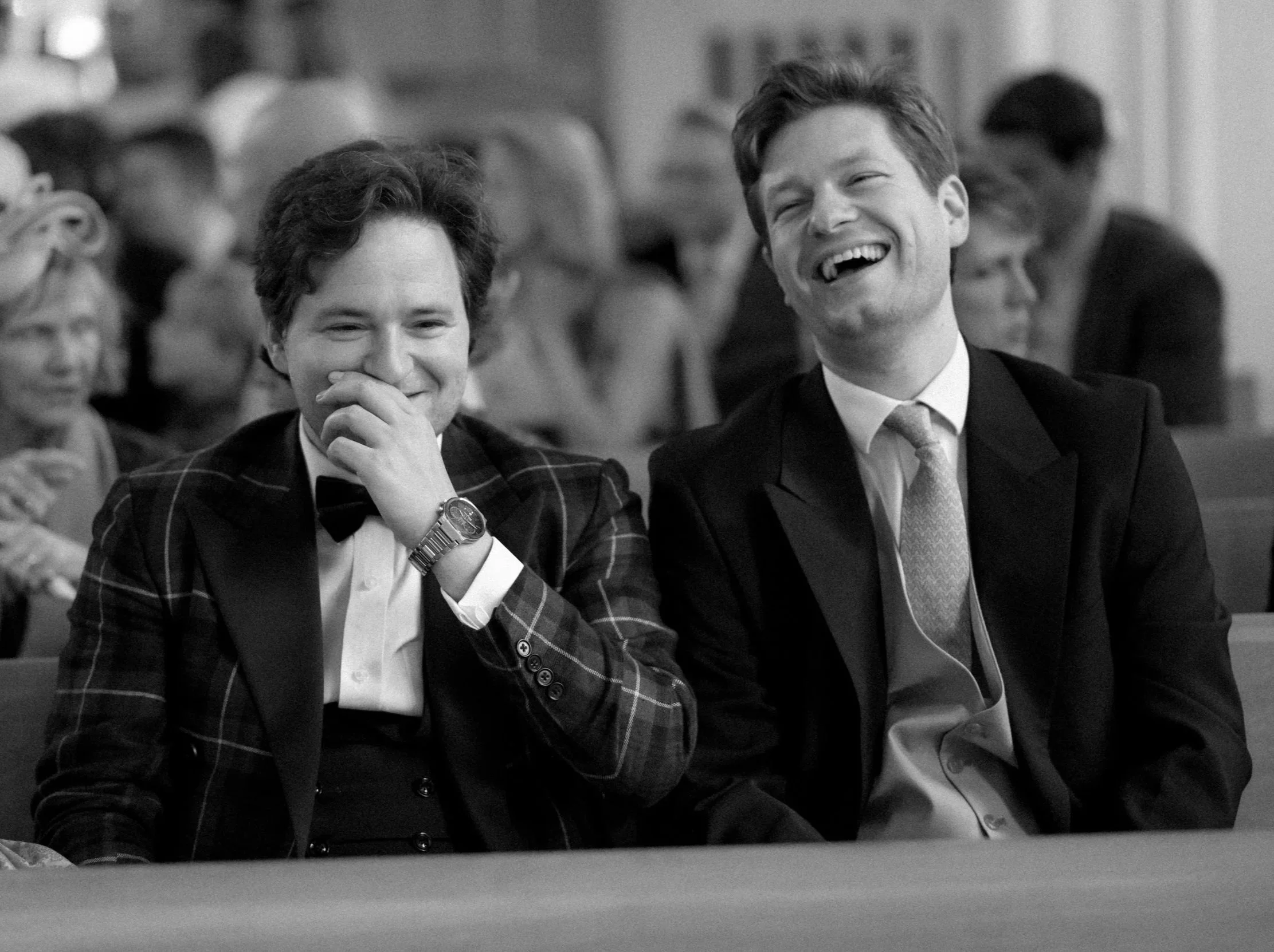 A black and white photograph at St Peter's Eaton Square of two white men, brothers laughing as they wait for their sister's wedding ceremony to begin. They are both in suits. The photograph feels joyful.