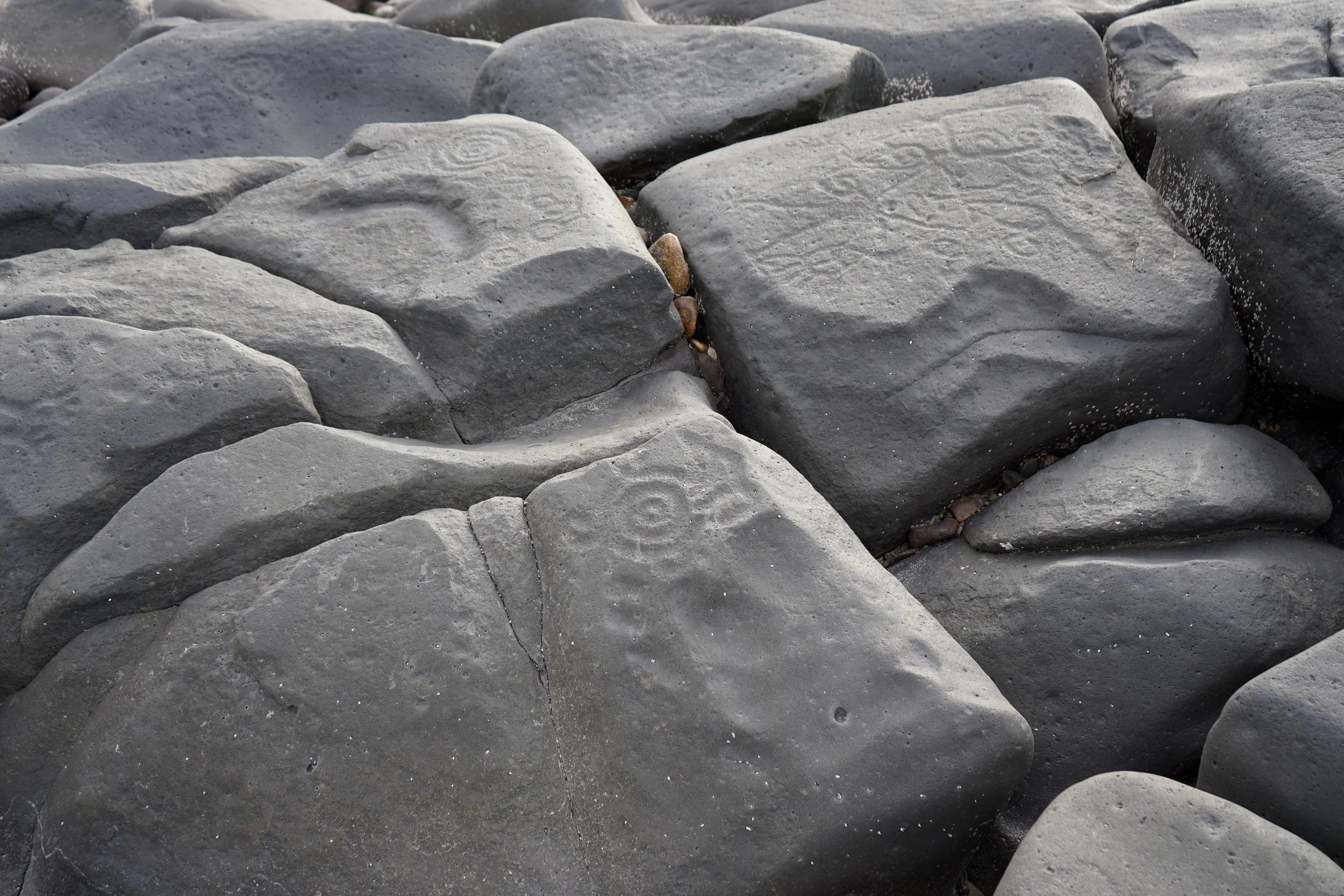 Close-up of large, smooth gray rocks with some etched patterns and small pebbles in the cracks.