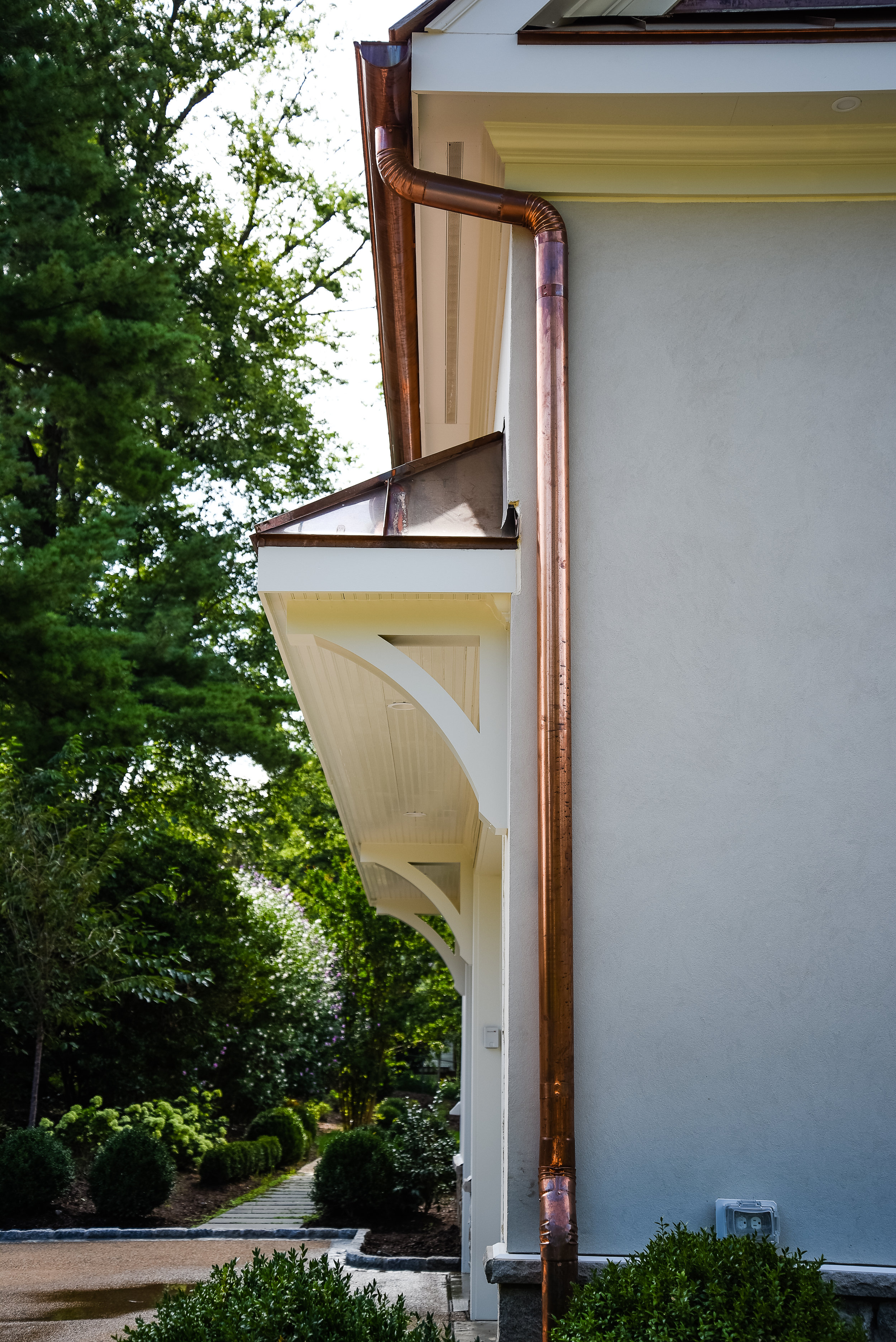 Round copper gutters &amp;and downspouts with a creamy white stucco and custom-built overhang with corbels for garage entry.
