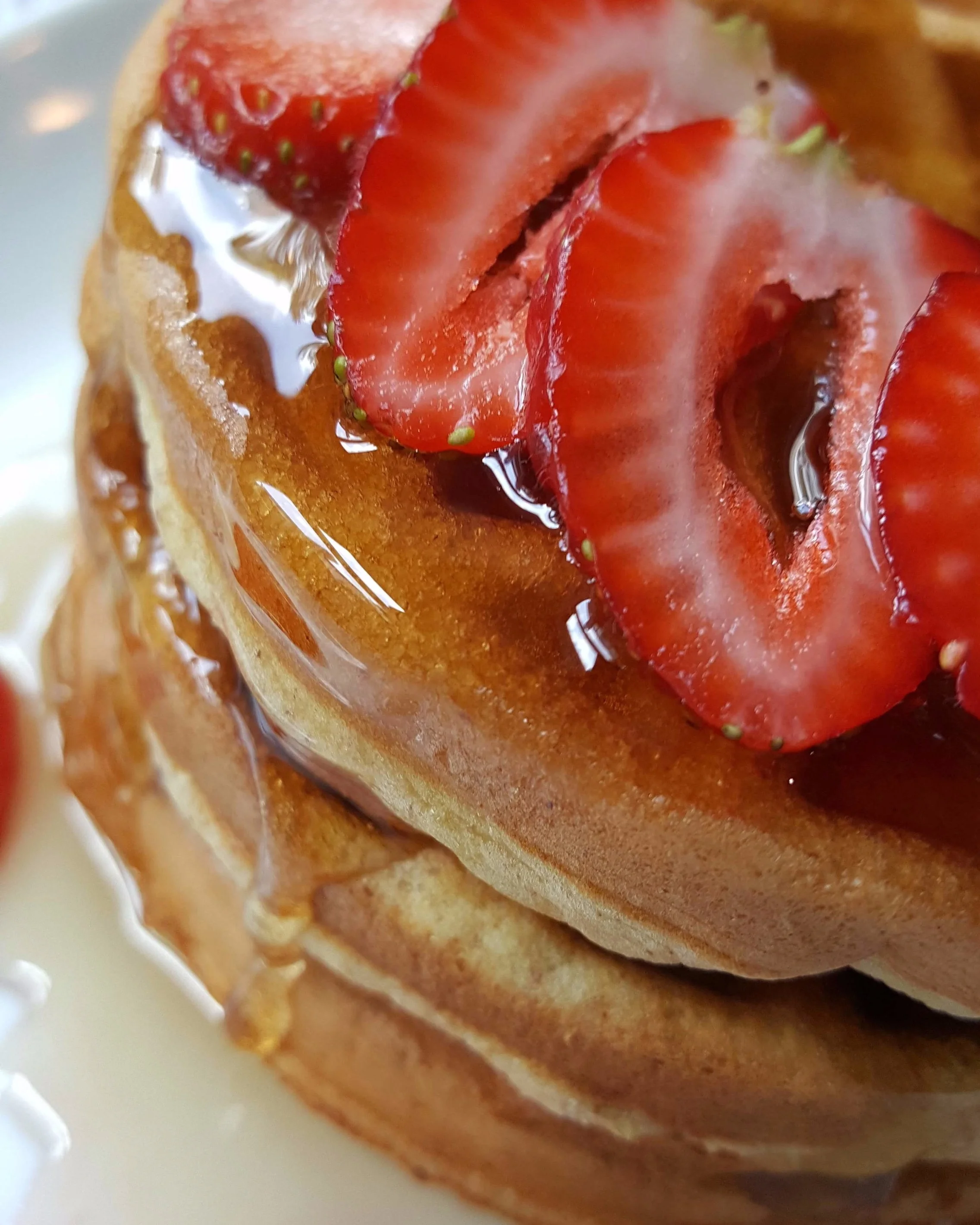 Keto waffles with one sliced strawberry and Keto friendly syrup.