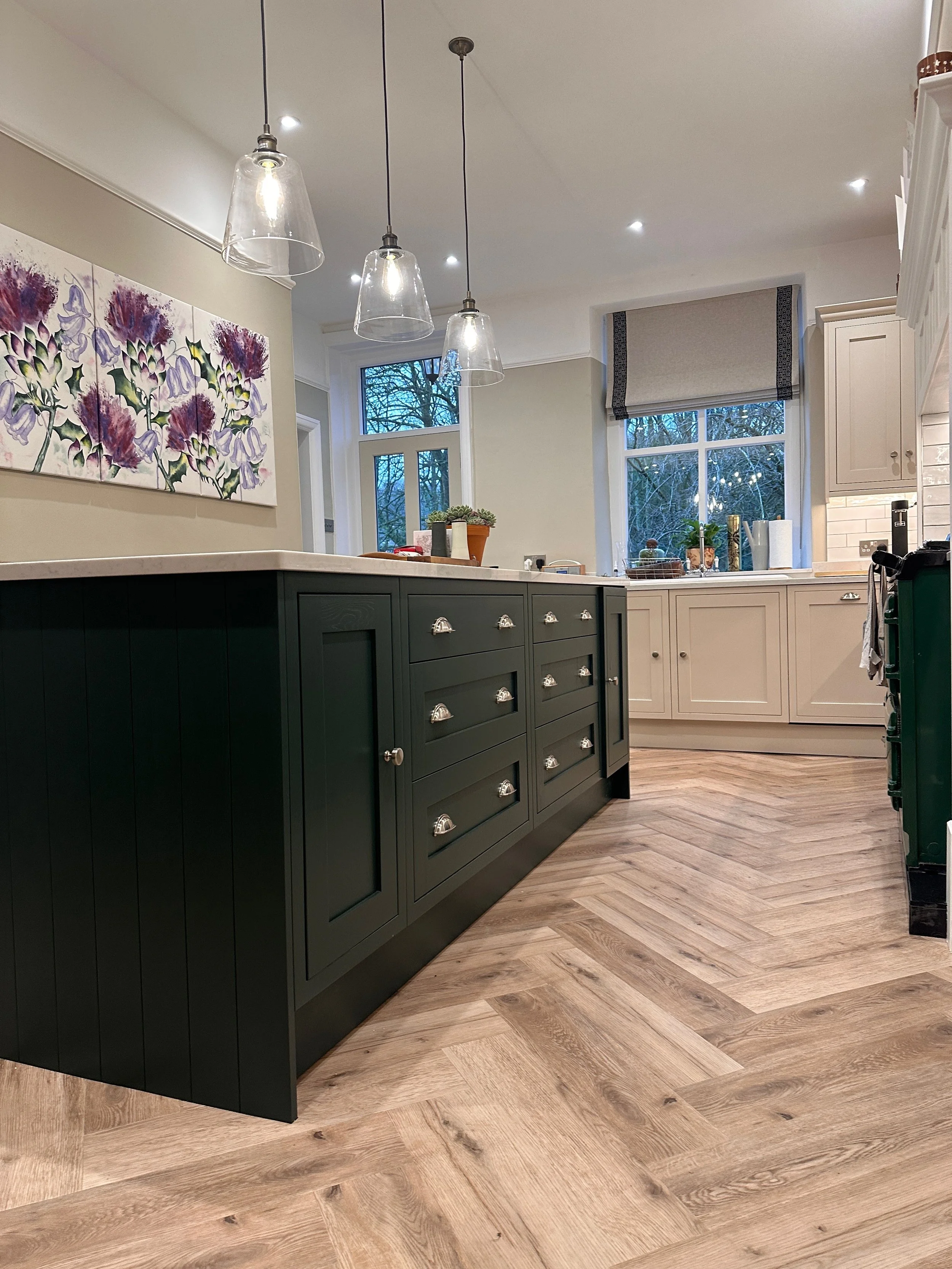 Modern kitchen with green island, white cabinets, wooden floor, and pendant lights.