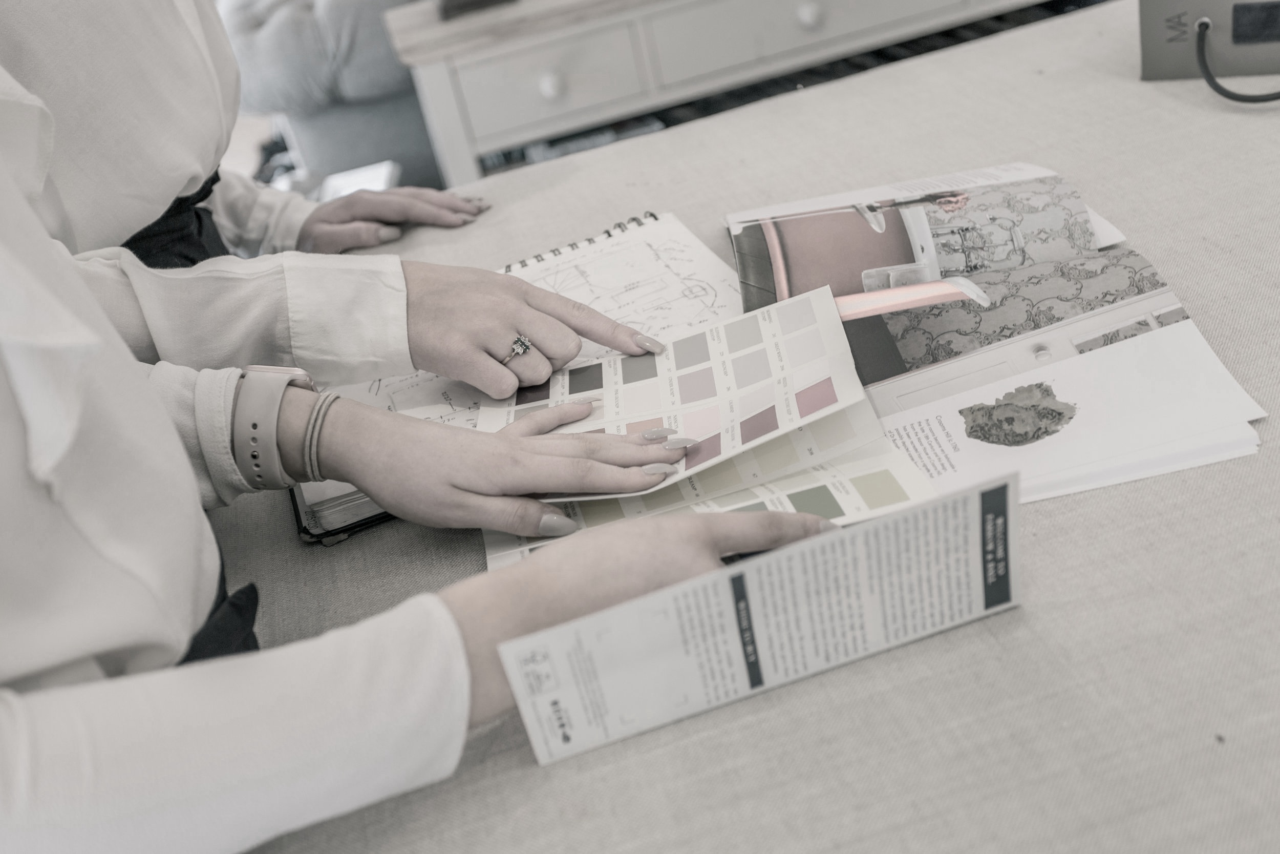 Two people are looking at fabric or color sample books and catalogs on a table, with their hands pointing at different pages.