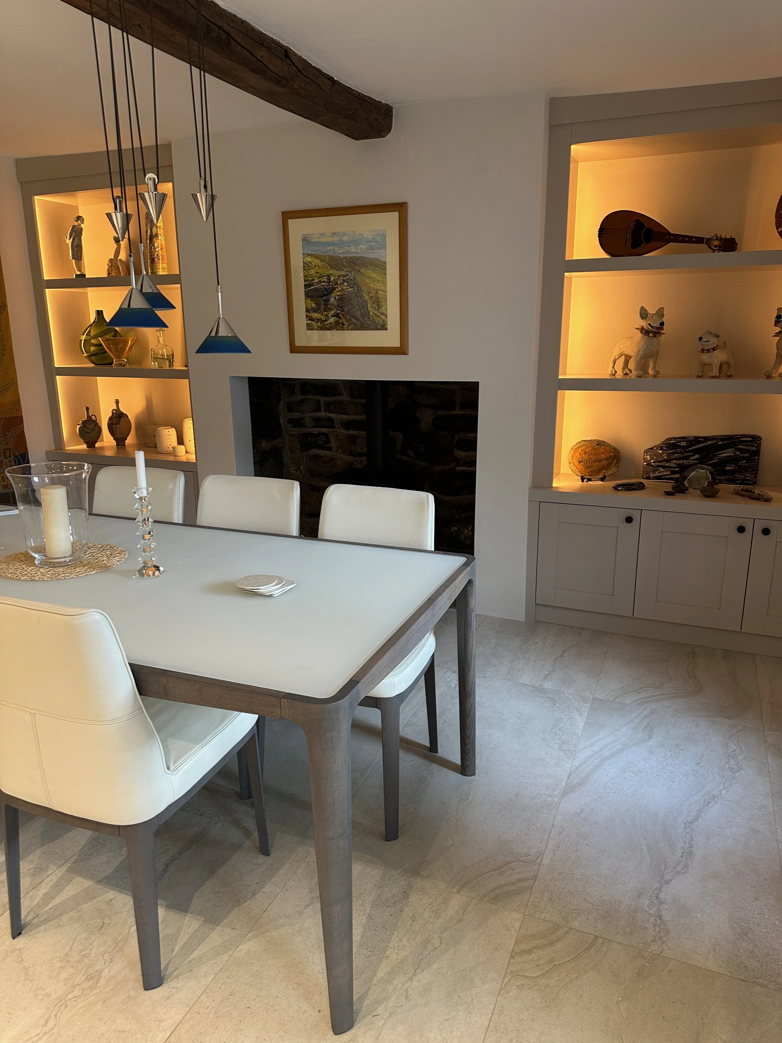 A dining room with a white table, cream chairs, a candle centerpiece, and built-in shelves with decorative objects and lighting.