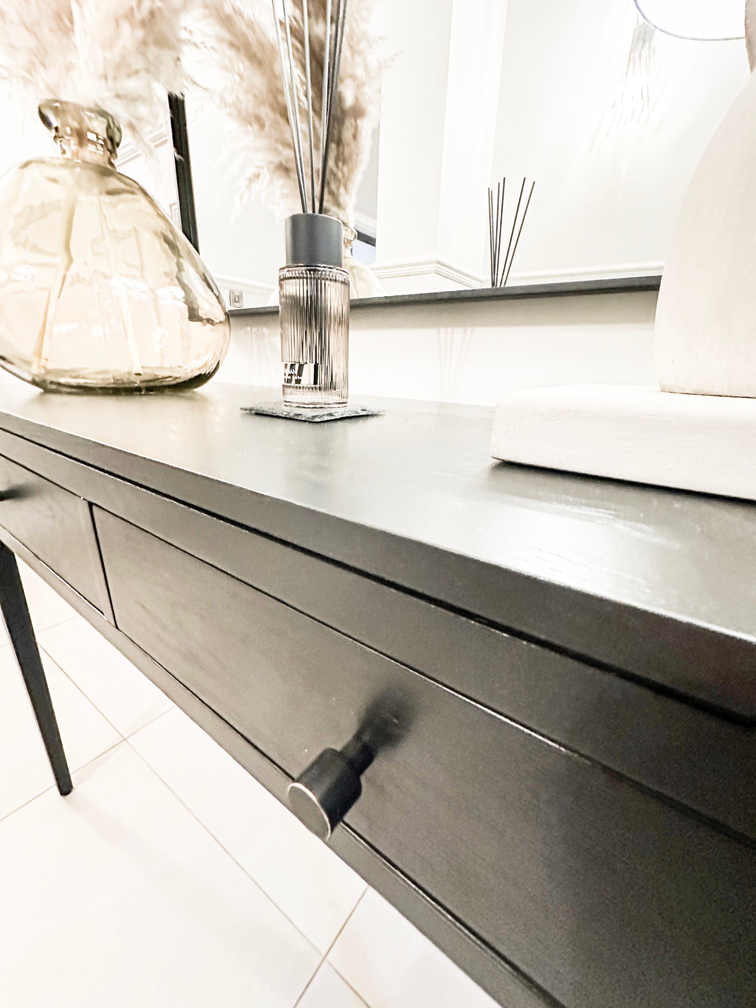 Close-up of a gray sideboard with decorative bottles and reed diffusers on top.